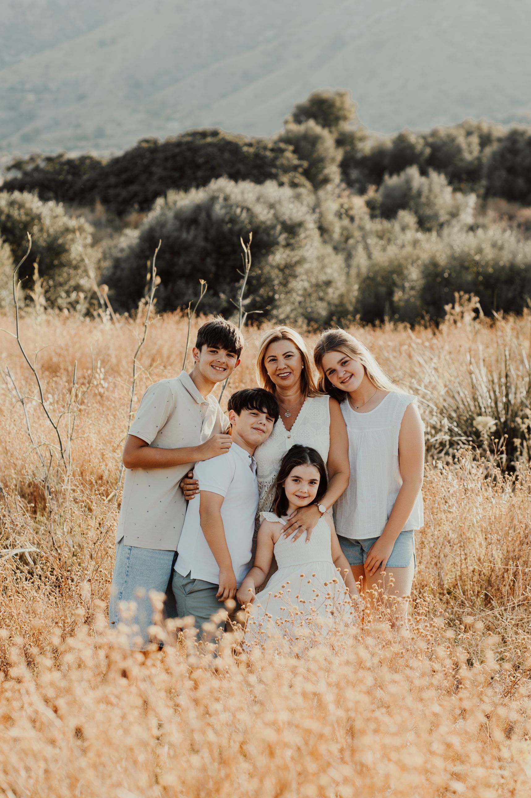 Familia posando en un campo soleado de hierba alta con colinas al fondo.
