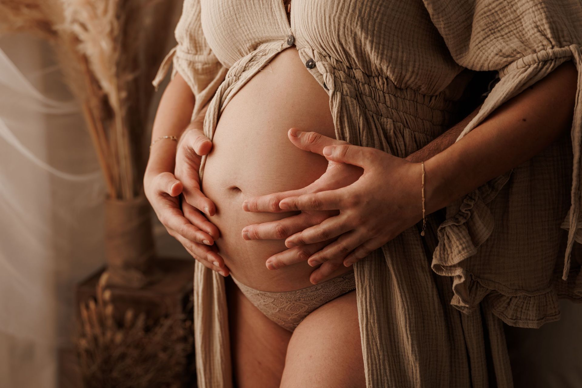 Unas manos acarician suavemente un vientre redondeado de embarazada, envuelto en una suave bata color beige.