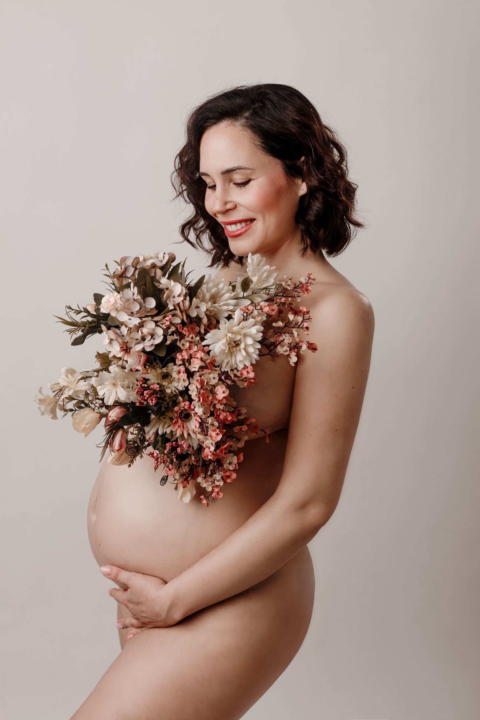 Mujer embarazada sosteniendo un ramo de flores sobre un fondo neutro.