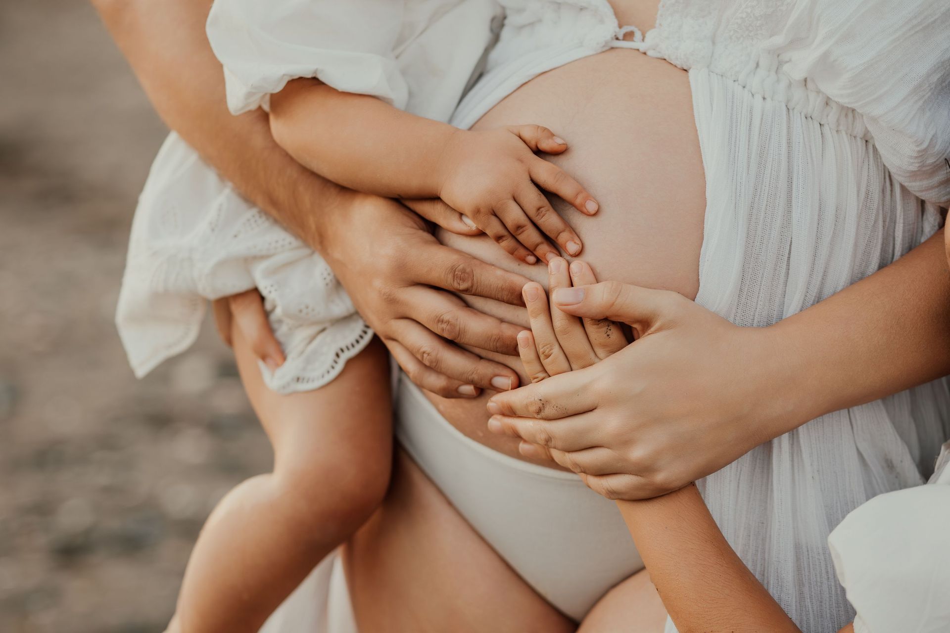 Vientre de embarazada acariciado suavemente por varias manos en tonos suaves y neutros.