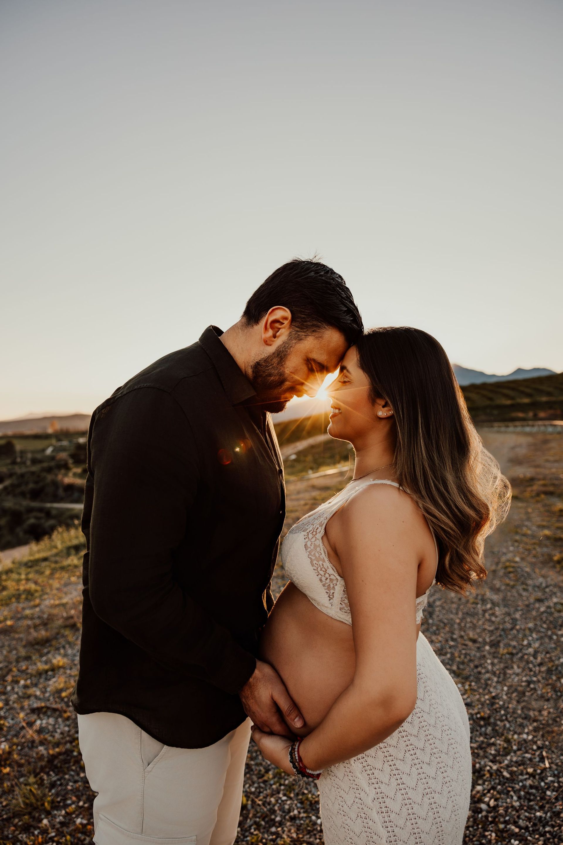 Una pareja de pie al aire libre al atardecer, con las frentes tocándose y las montañas de fondo.