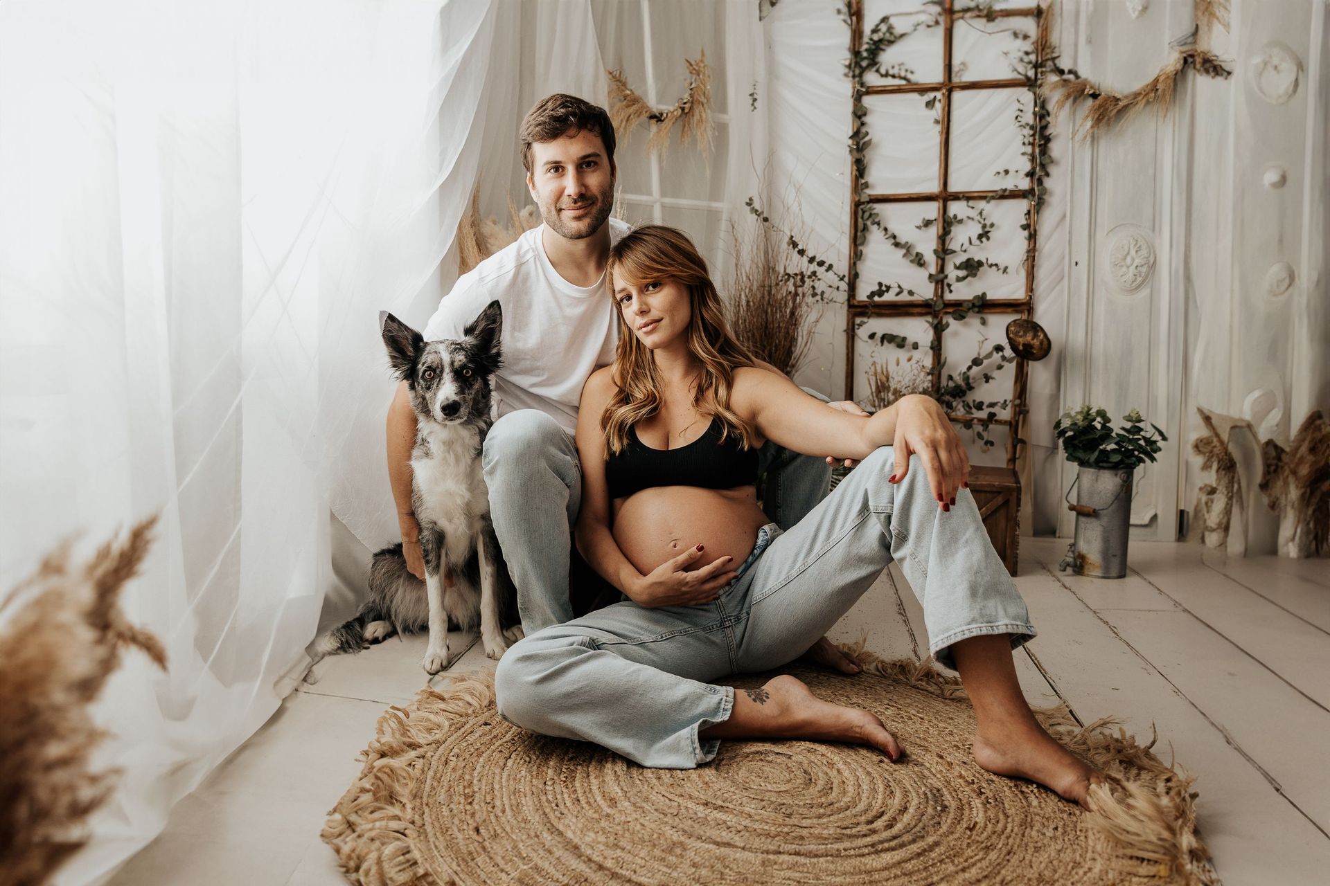 Una pareja con su perro sentada en un acogedor estudio de estilo bohemio con cortinas suaves y decoración tejida.