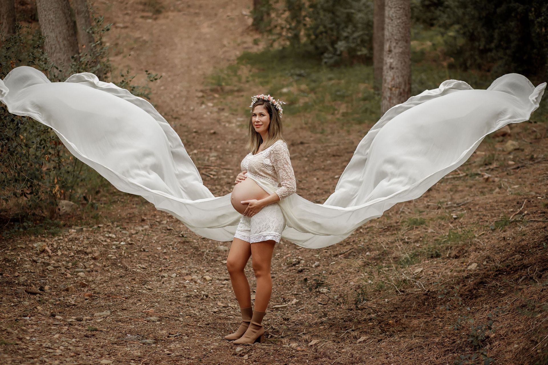 Mujer con un vestido blanco de pie al aire libre con grandes alas de tela blanca ondeando detrás de ella.