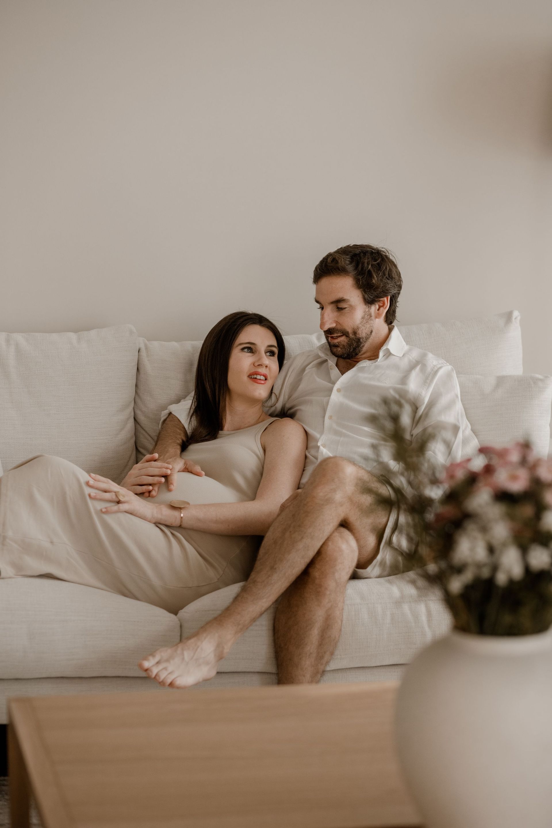 Una pareja sentada en un sofá claro en una sala de estar luminosa, conversando en voz baja.