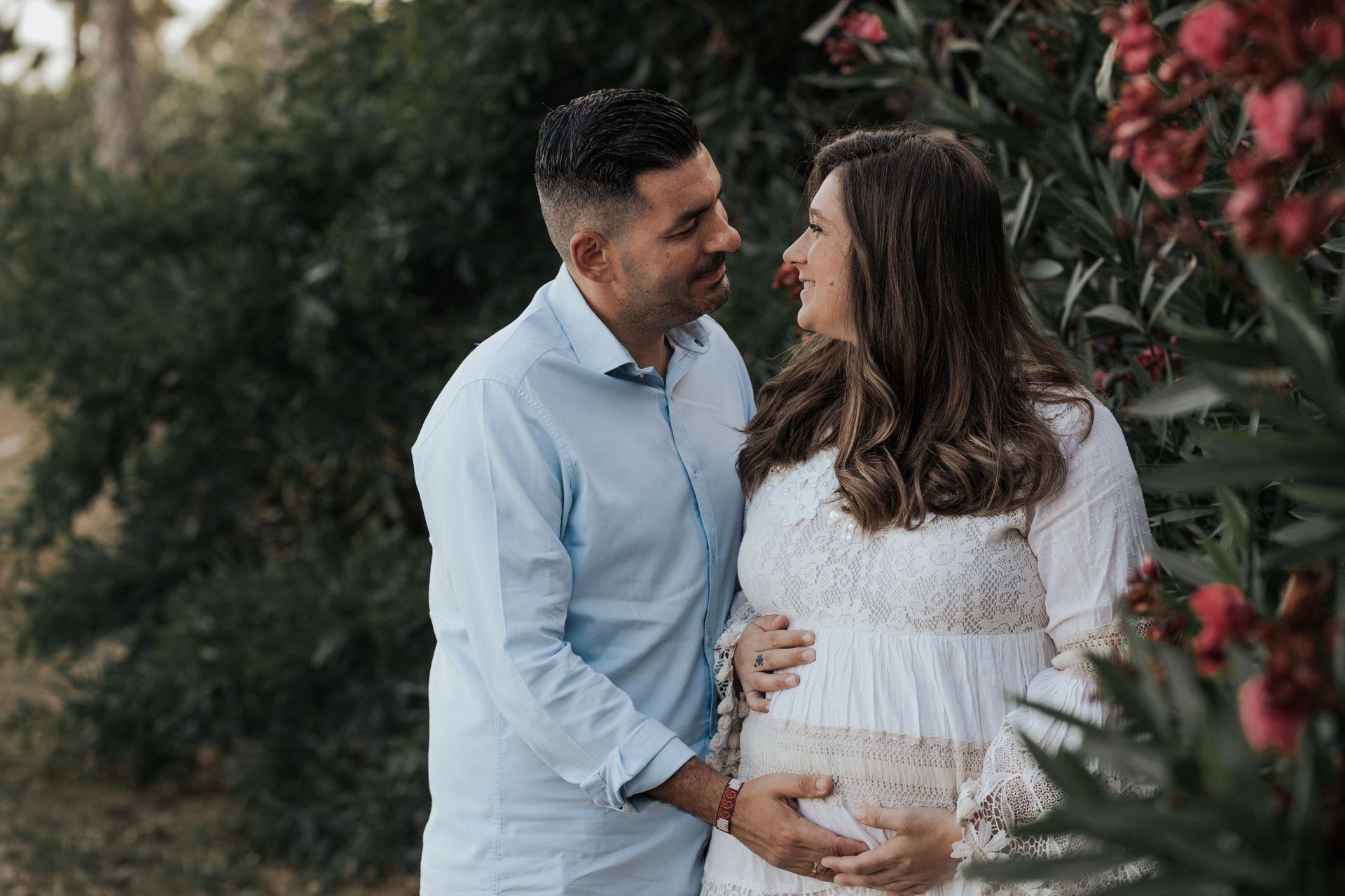 Una pareja al aire libre, sonriendo y abrazándose, con la mujer sosteniendo una barriga de embarazada.