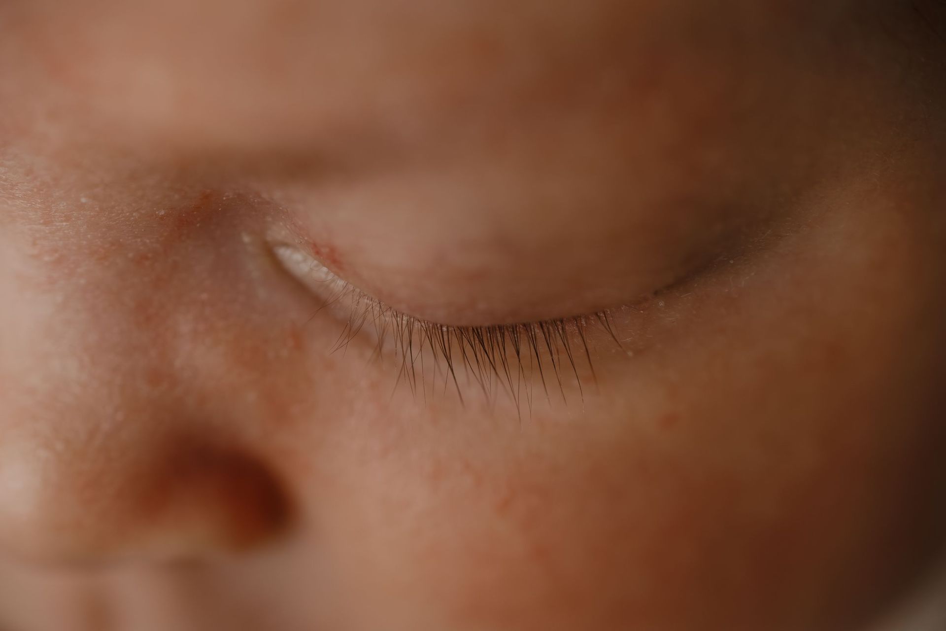 Primer plano de un rostro dormido con un ojo cerrado y tonos de piel suaves y marrones.