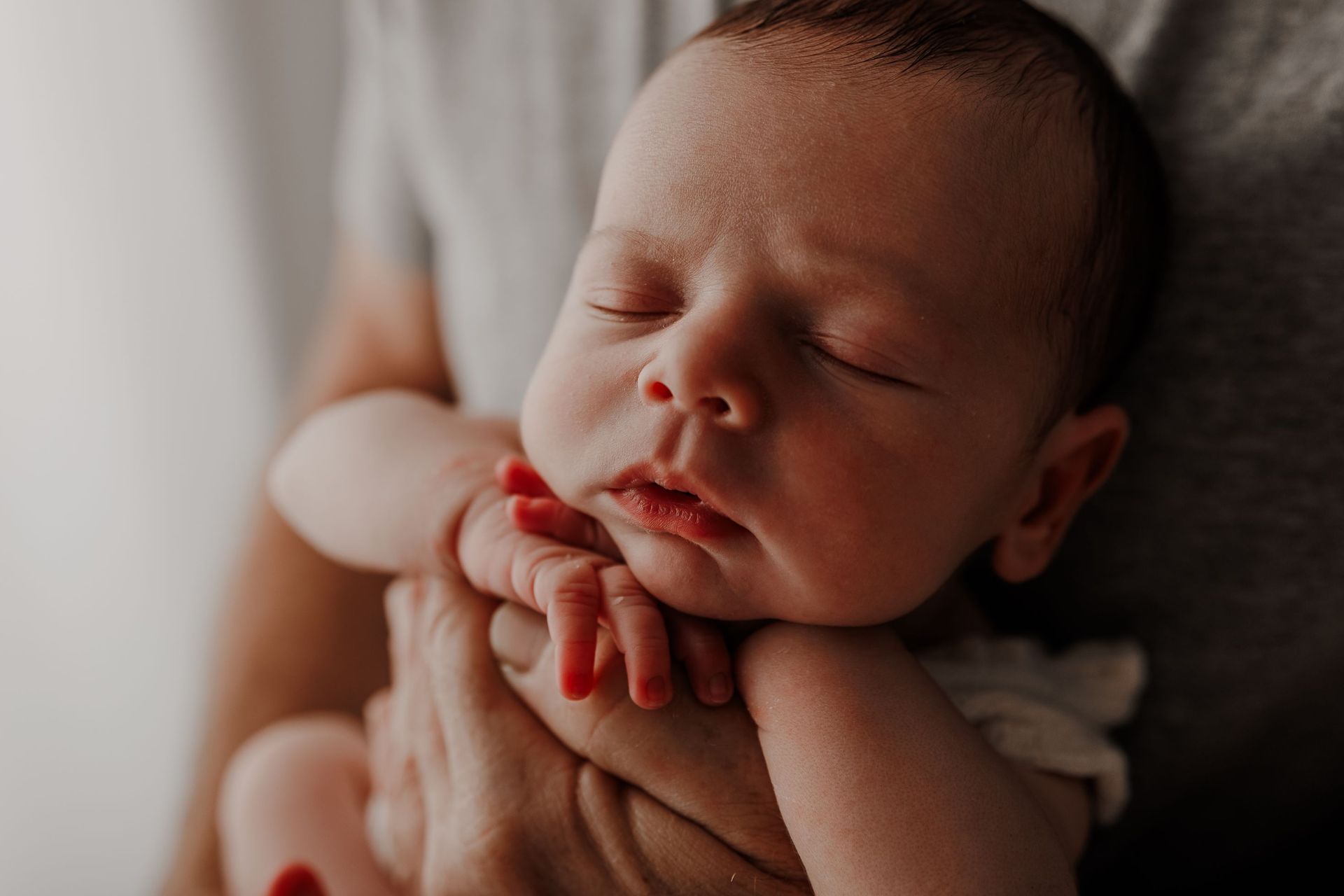 Un recién nacido durmiendo, descansando en manos de un adulto, con una suave luz natural y una expresión serena.