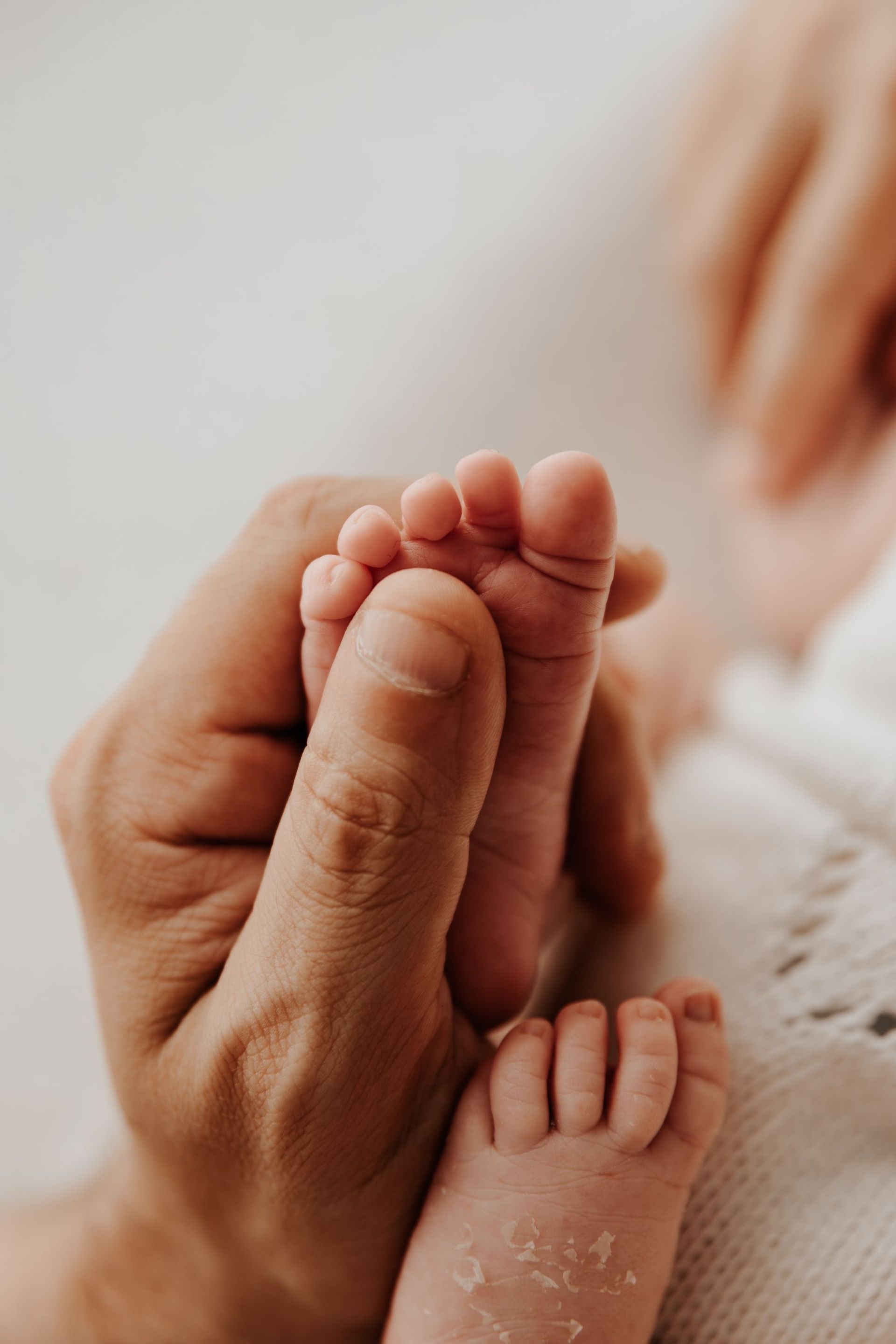 Una mano adulta sostiene suavemente el pie de un bebé sobre una manta suave.