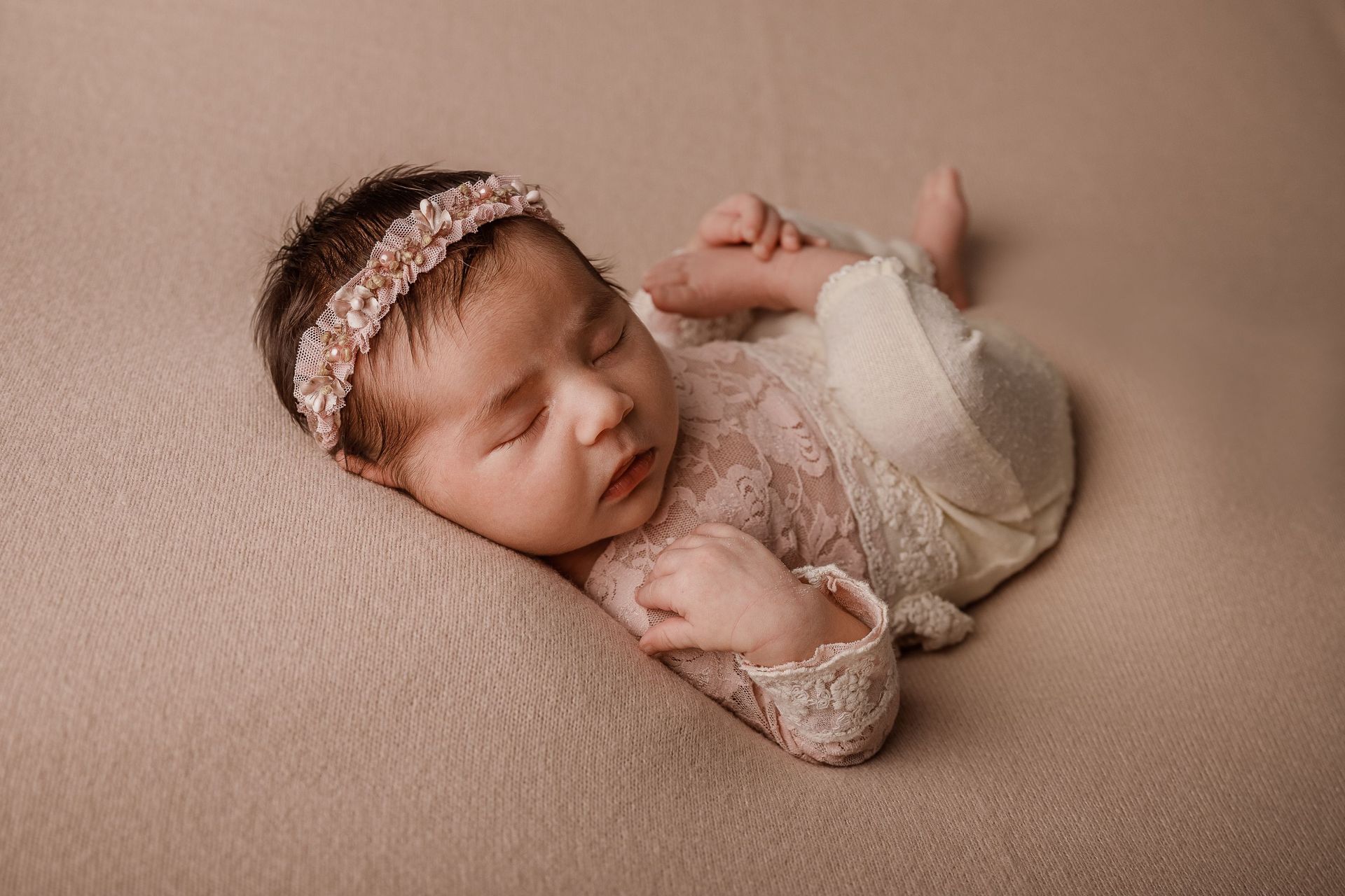 Bebé durmiendo con un conjunto de encaje y una diadema, descansando sobre una suave manta beige.