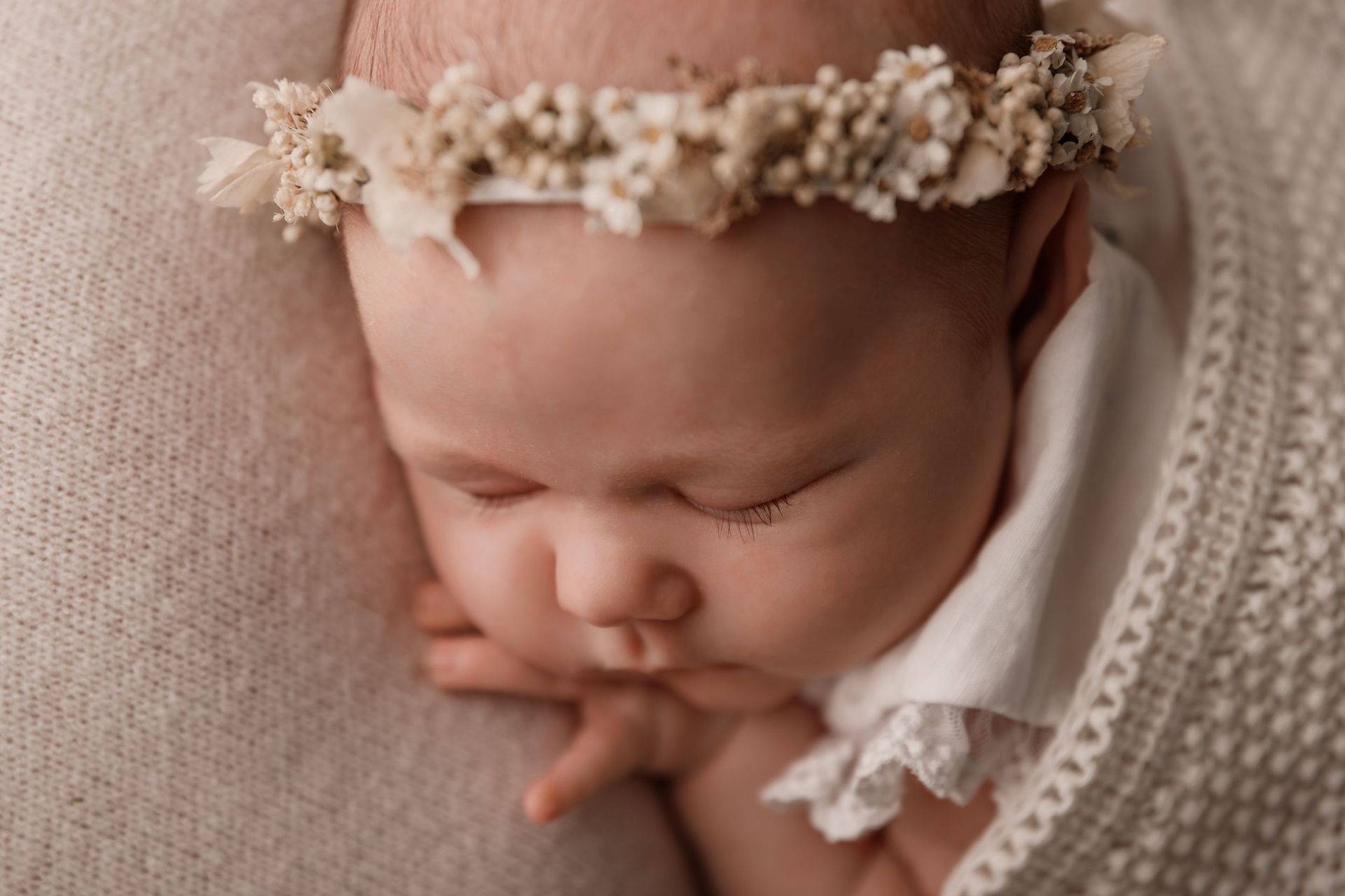 Bebé durmiendo con una diadema floral, descansando sobre una suave manta de punto.