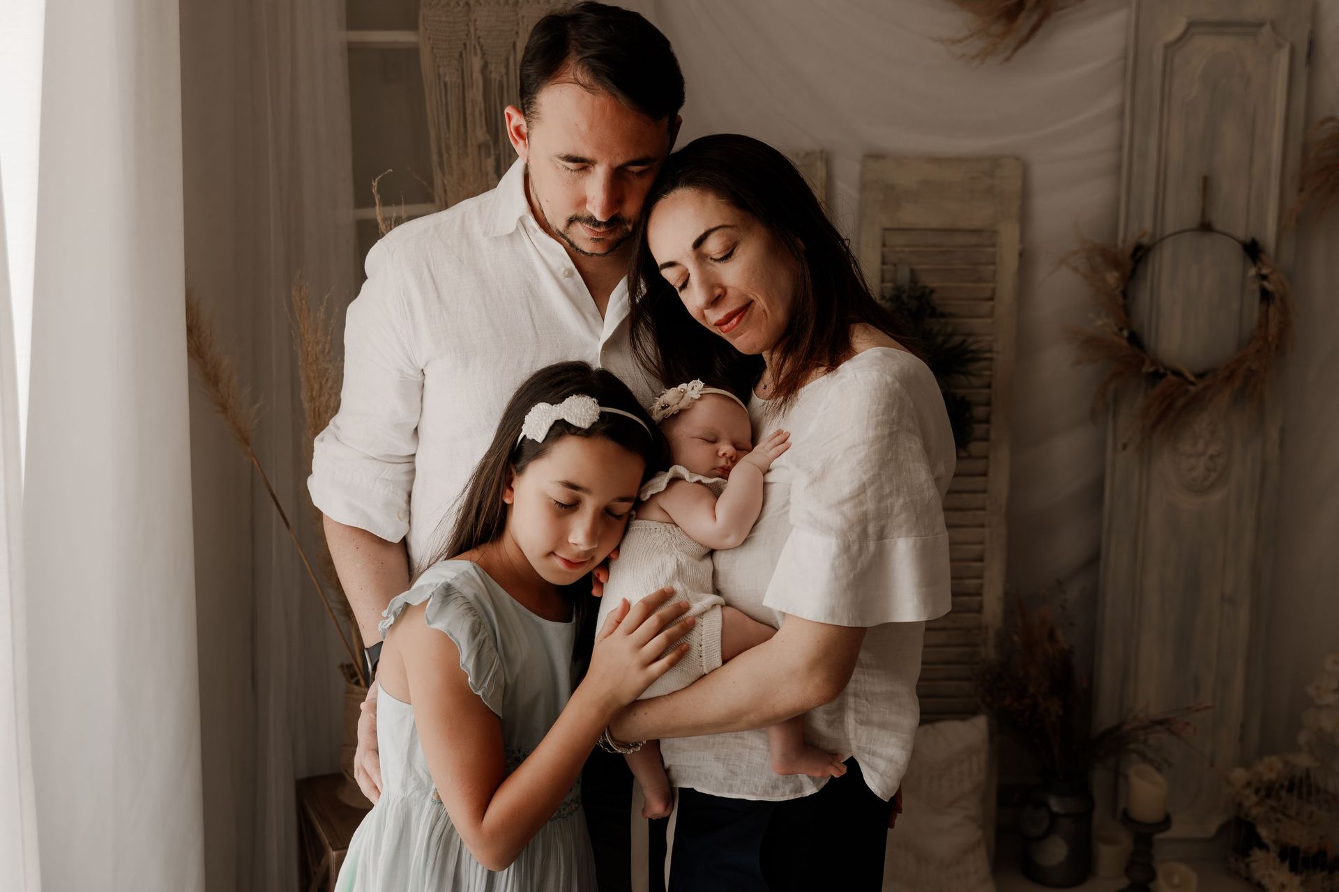 Familia de cuatro personas posando en el interior; los padres abrazan a dos niños vestidos con ropa de color beige suave.