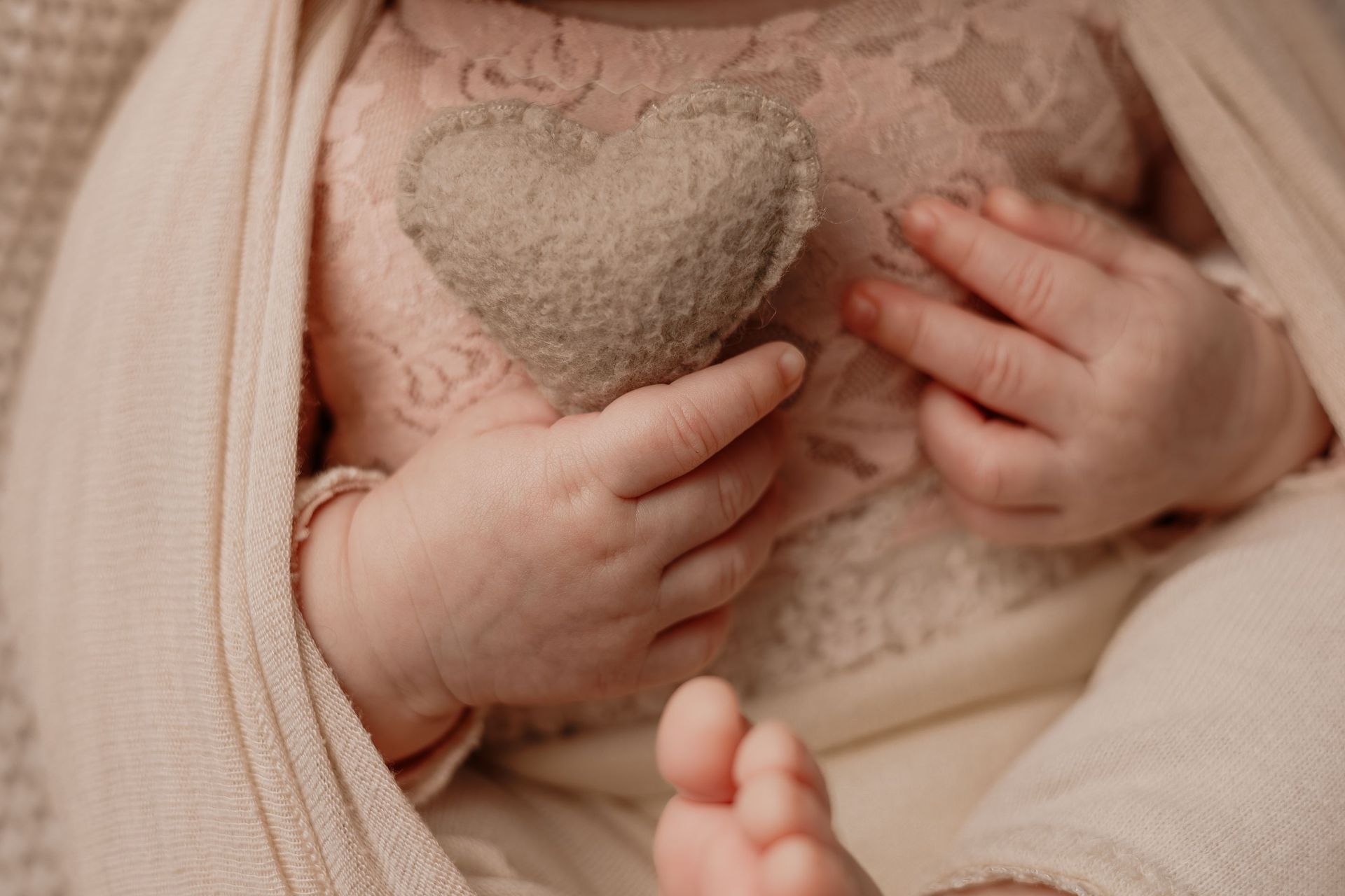 Un bebé sostiene un suave juguete con forma de corazón, envuelto en una manta beige.