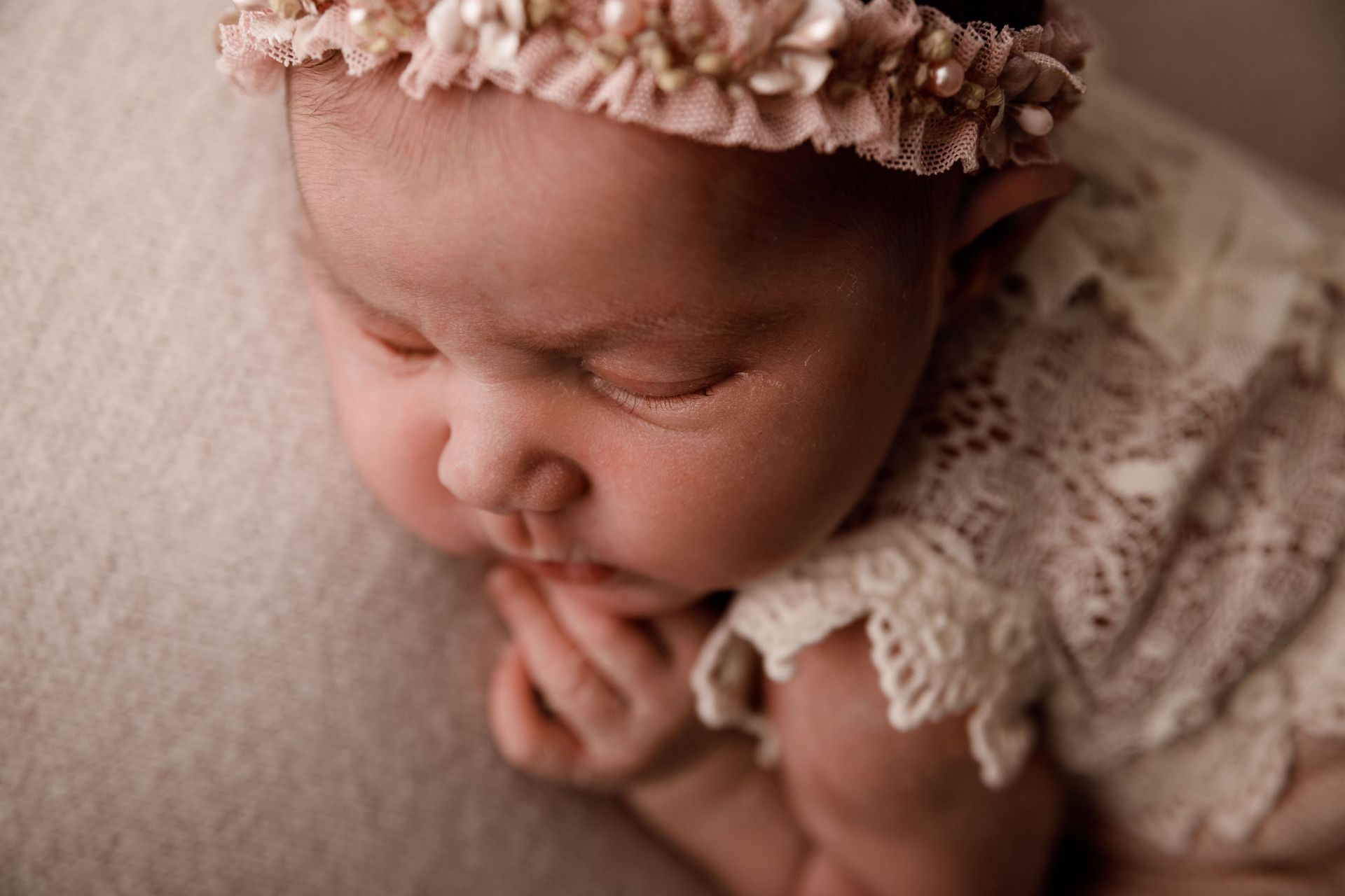 Bebé durmiendo con un conjunto de encaje color crema y una diadema floral, descansando sobre una suave manta beige.