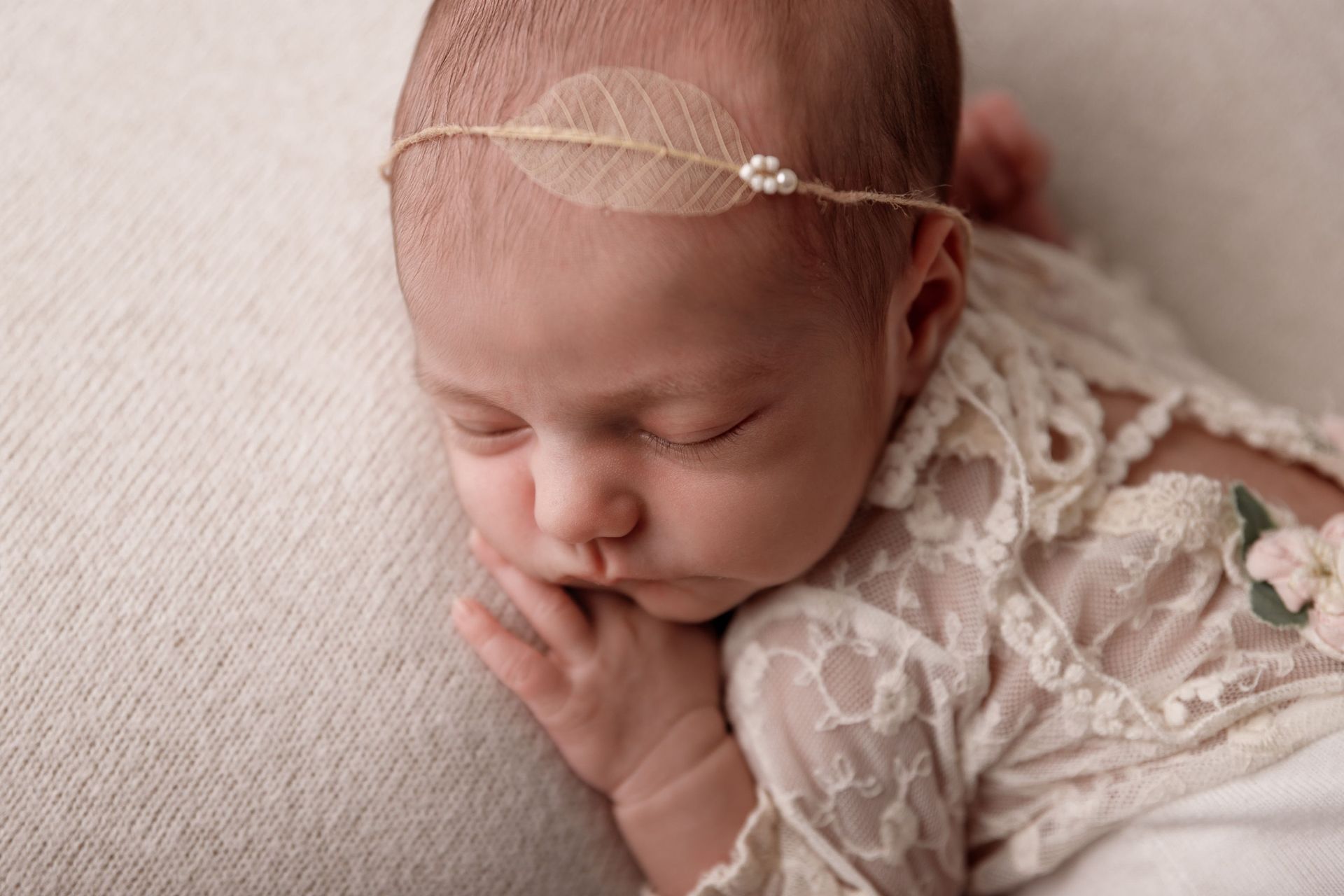 Bebé durmiendo con un conjunto de encaje color crema y una diadema, descansando sobre una suave manta beige.