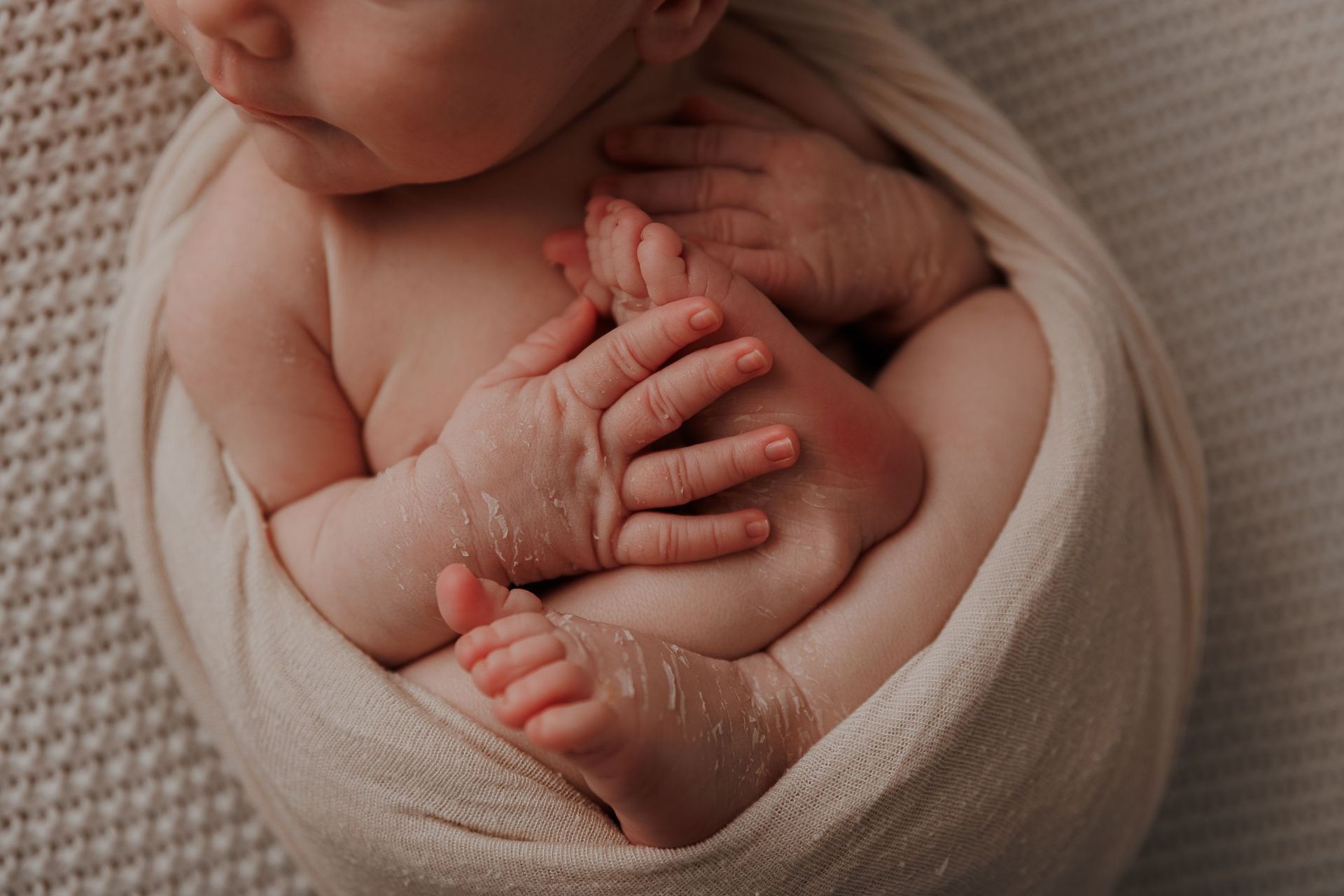 Un recién nacido envuelto en una manta beige, con sus pequeños pies y manos pegados al cuerpo.
