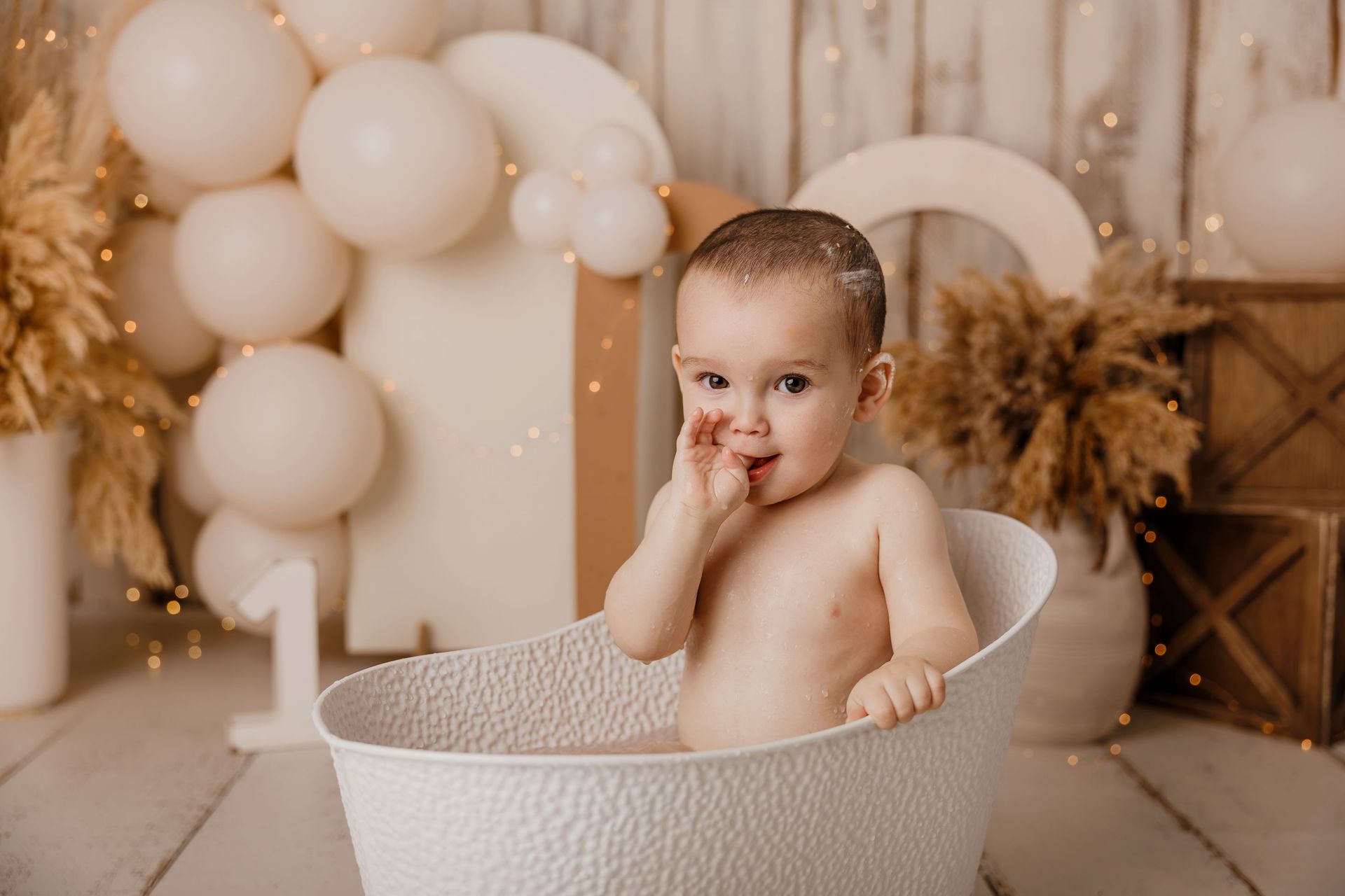 Bebé en una bañera blanca en una fiesta de primer cumpleaños decorada con globos y un gran número 1.