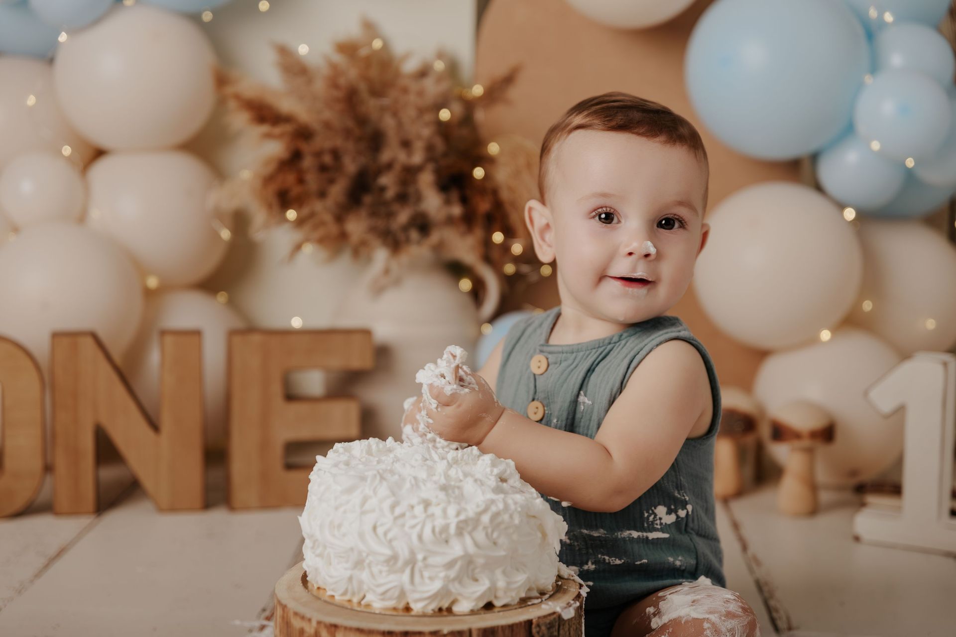 Un niño pequeño con un mono vaquero posa junto a una tarta de cumpleaños decorada con globos.