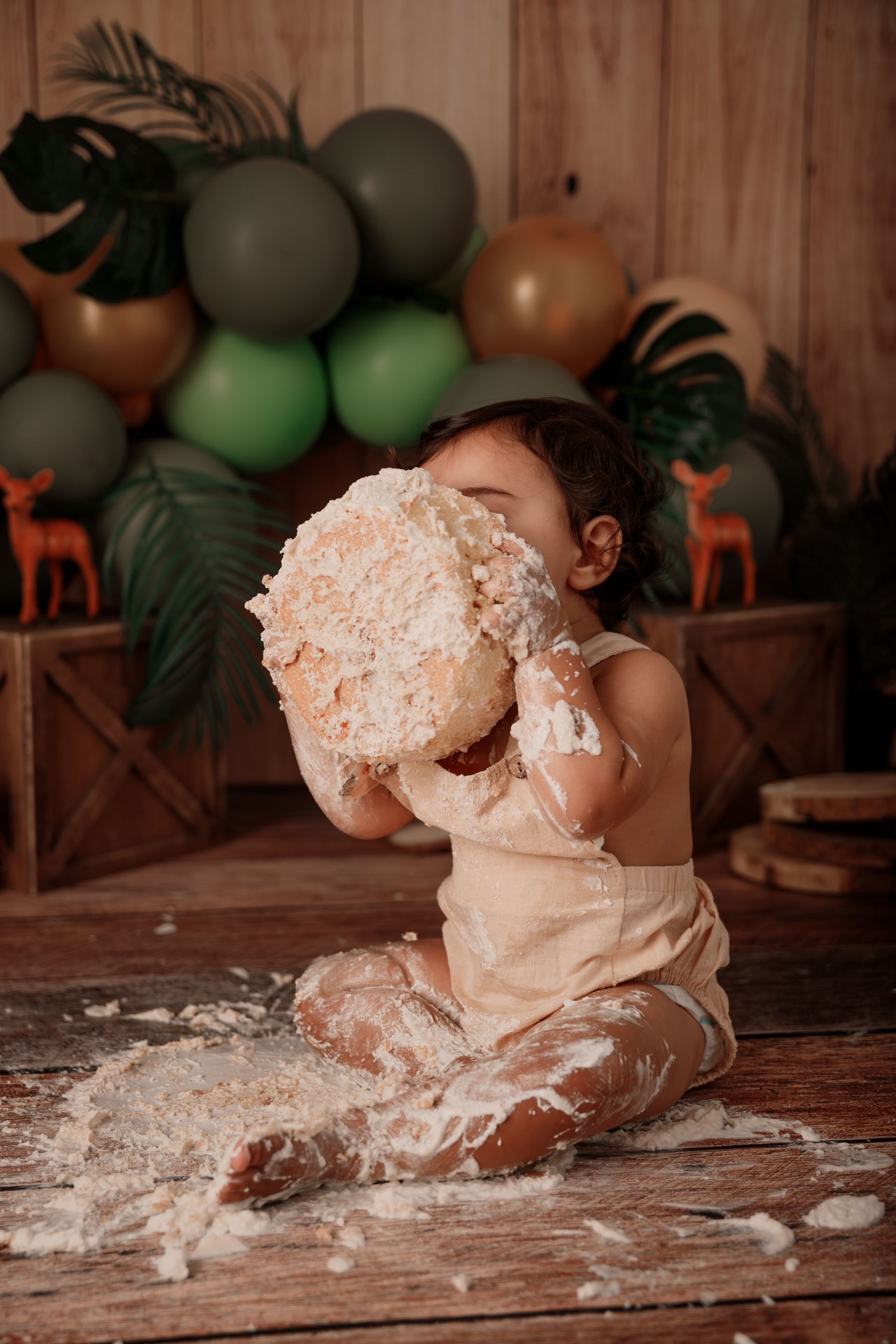 Un niño pequeño sentado en un escenario para una sesión de fotos con pastel, cubierto de glaseado, con globos.