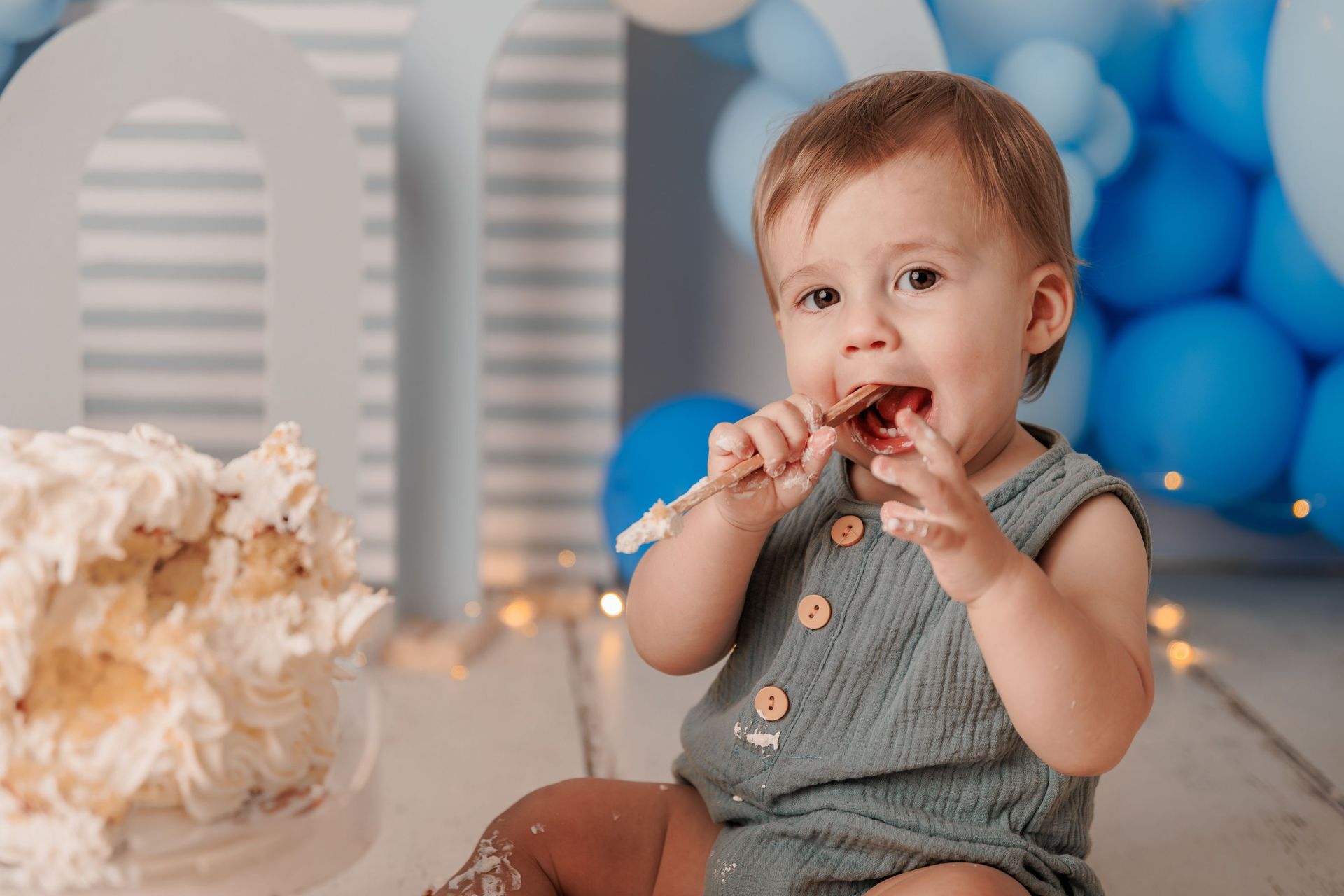 Un niño pequeño come pastel entre globos azules en una fiesta de cumpleaños.