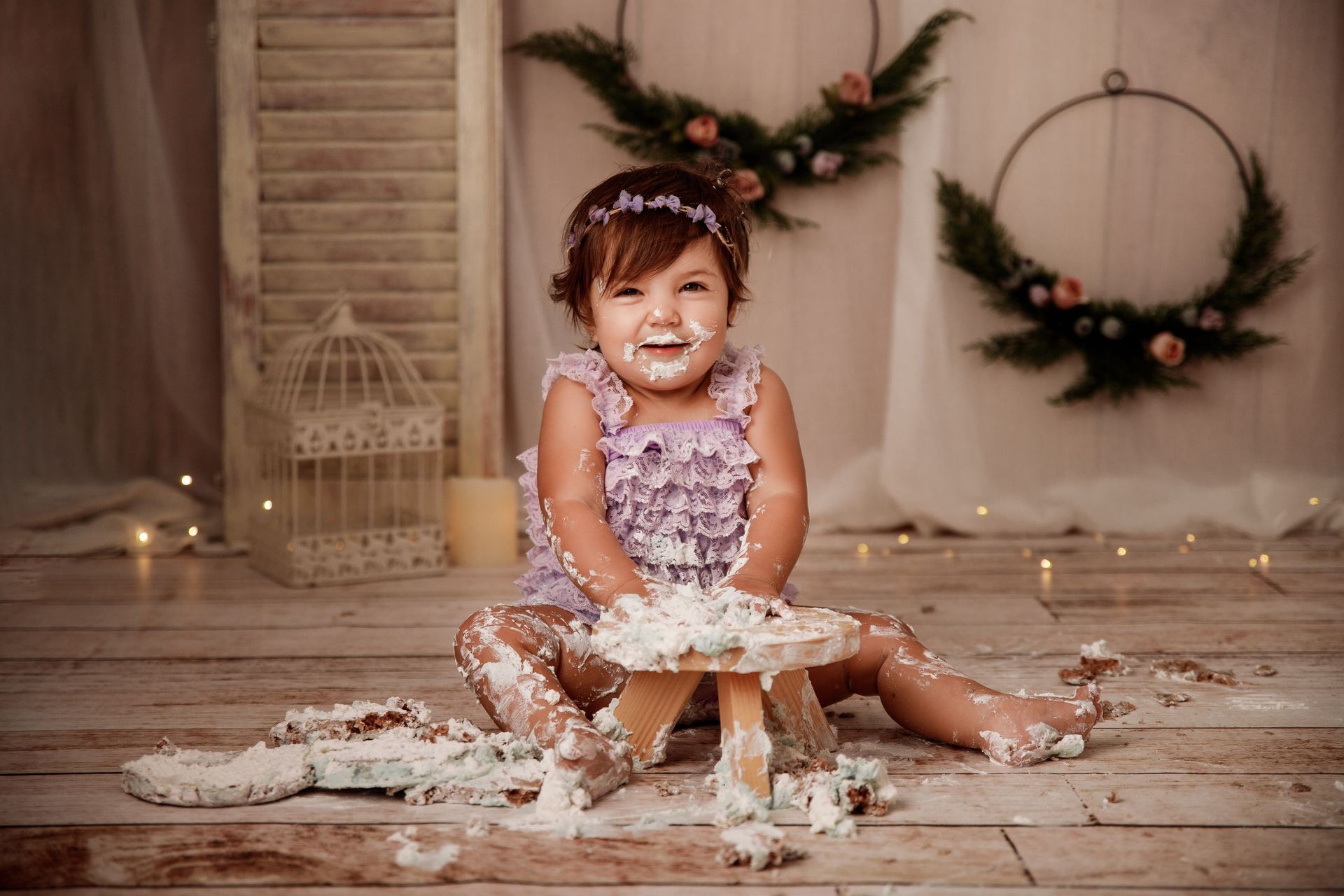 Niña sonriente con vestido de flores sentada en un suelo cubierto de pastel en un acogedor estudio.