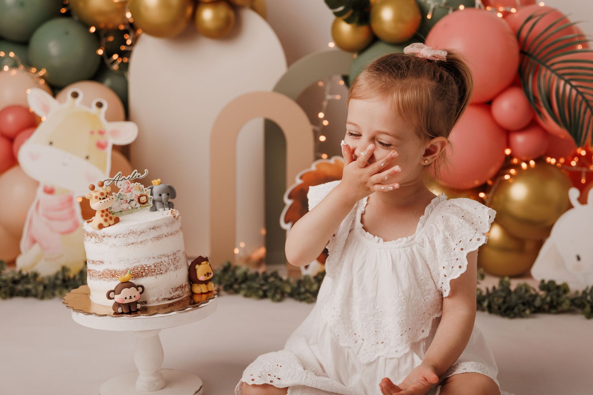 Un niño junto a una tarta de cumpleaños decorada en una fiesta con globos de colores pastel, intentando coger un dulce.
