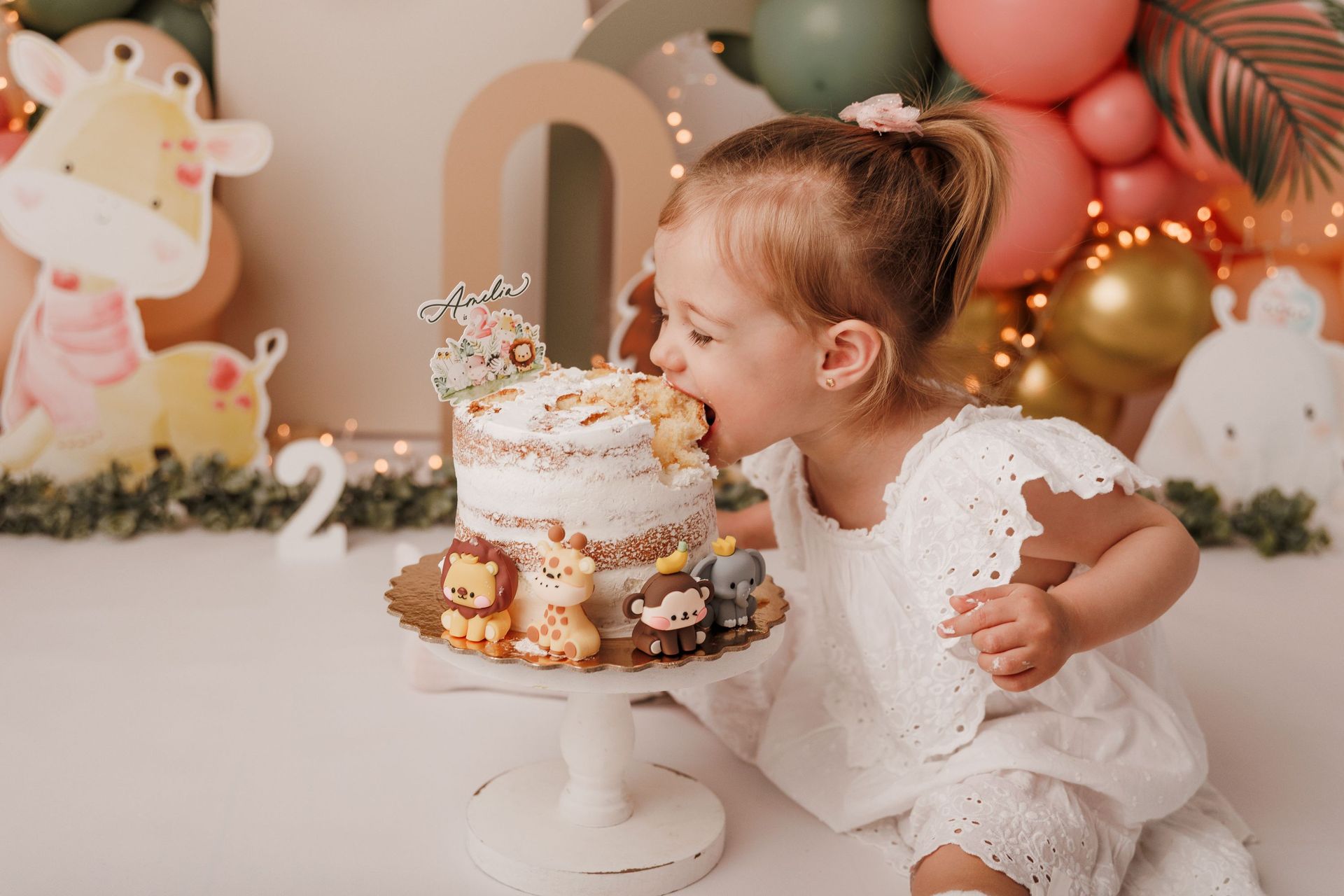 Una niña pequeña con un vestido blanco se inclina hacia un pastel de cumpleaños