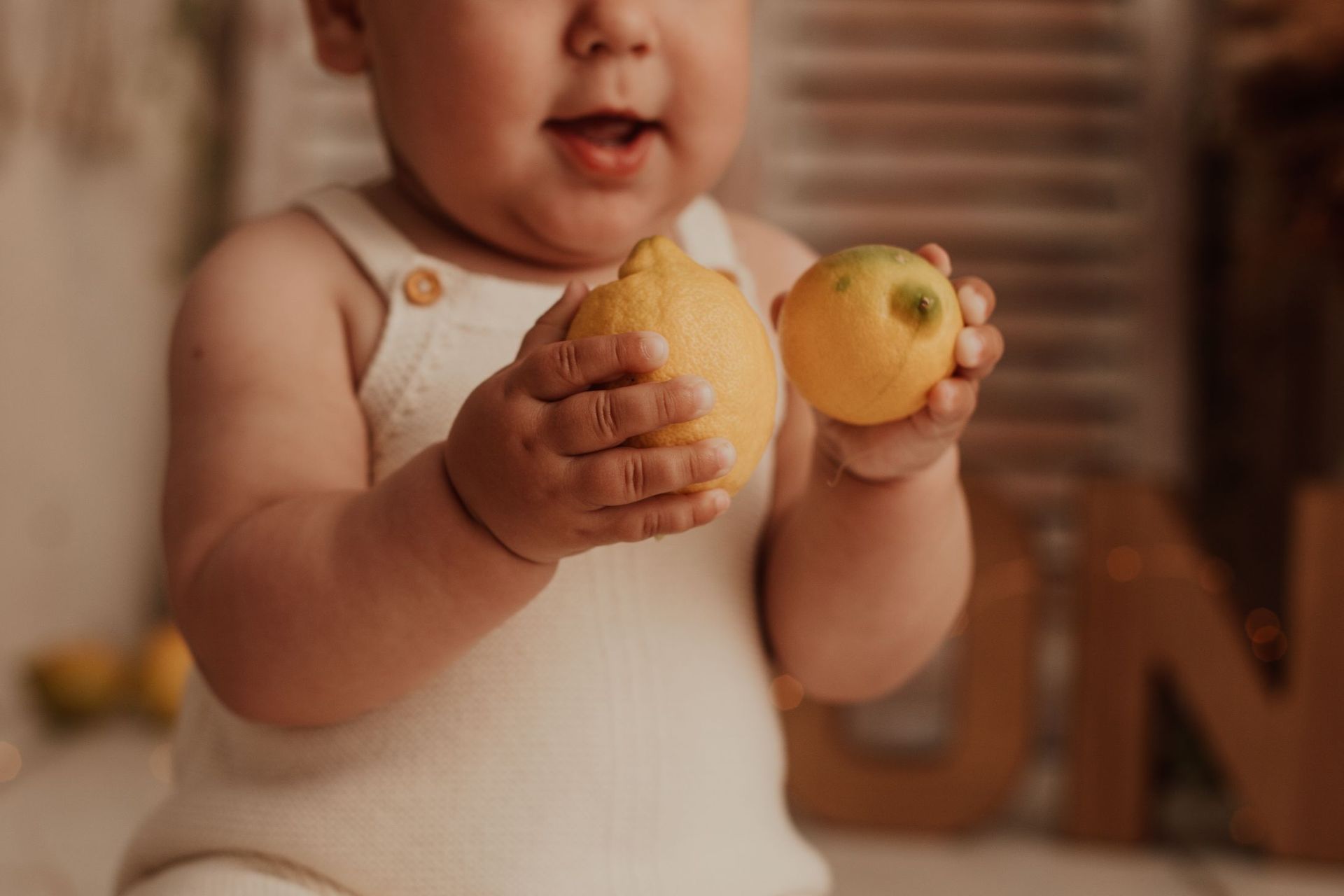 Bebé con un body blanco sosteniendo dos manzanas amarillas en el interior.
