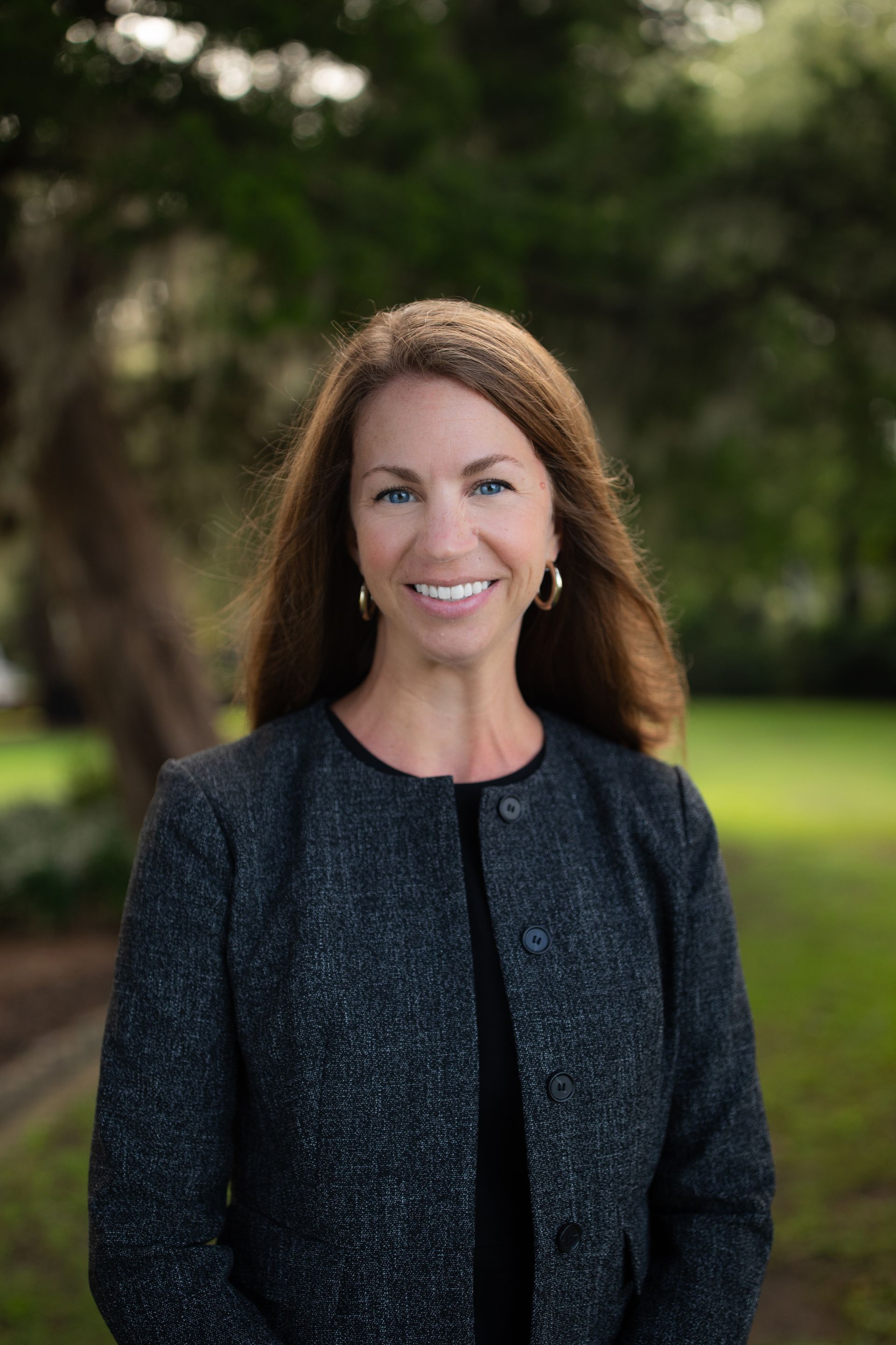 A woman in a gray jacket and earrings is smiling for the camera.