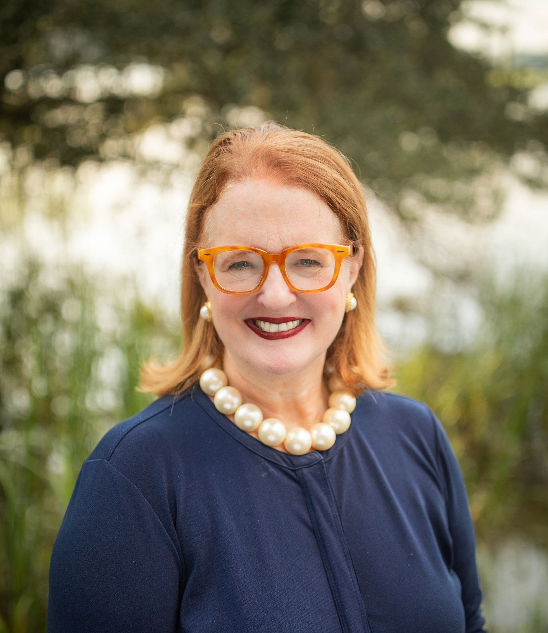 A woman wearing glasses and a black jacket is smiling for the camera.
