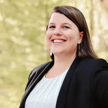 A woman in a black jacket and white shirt is smiling for the camera.