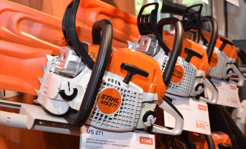 Eine Reihe orangefarbener und weißer Stihl-Kettensägen mit Preisschildern stehen in den Regalen eines Ladens.