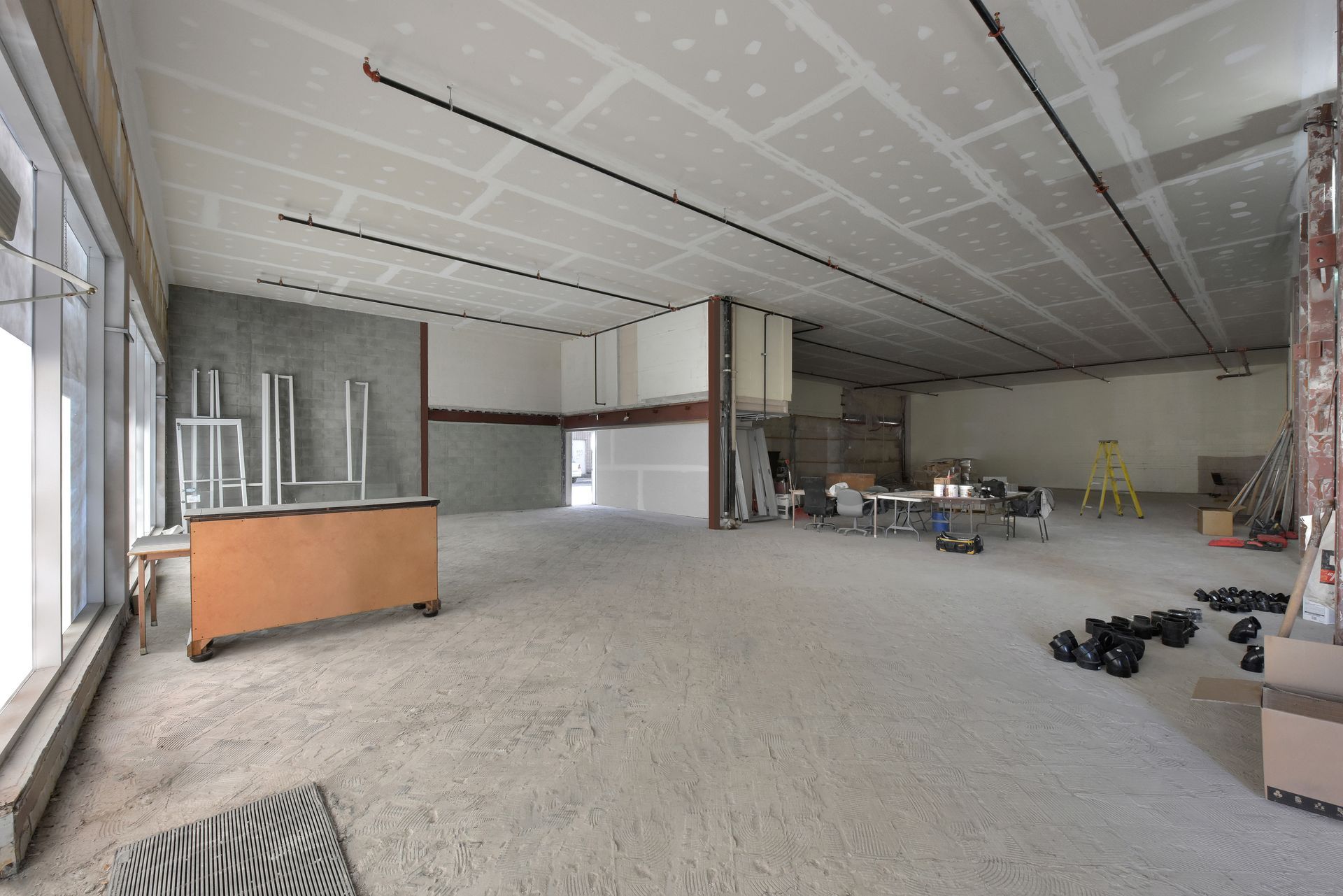 Intérieur d'une pièce en construction, avec poutres apparentes au plafond et murs non finis.
