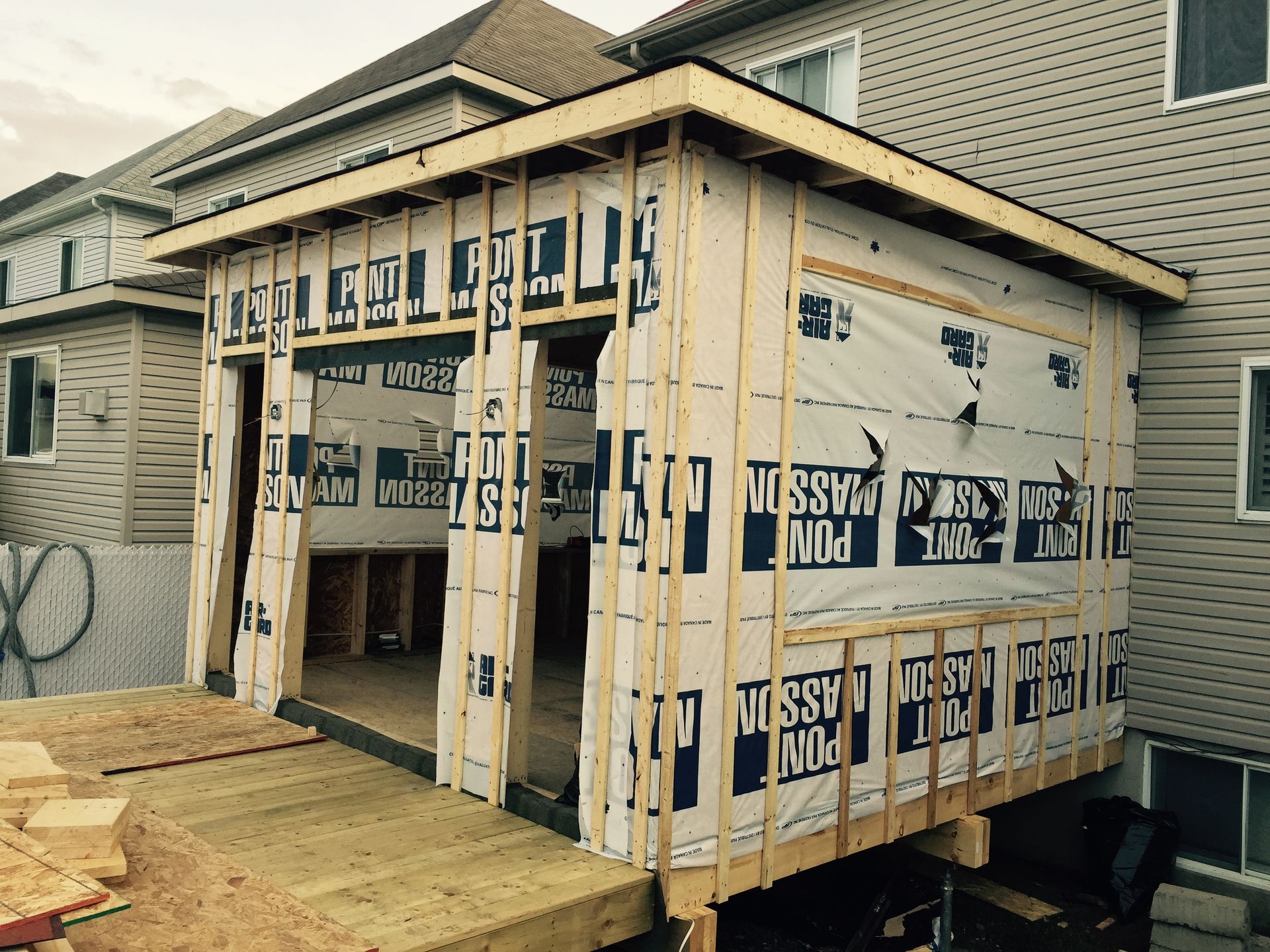 Vue extérieure d'un bâtiment en construction, montrant une charpente en bois, un revêtement et une toiture partiellement construite.