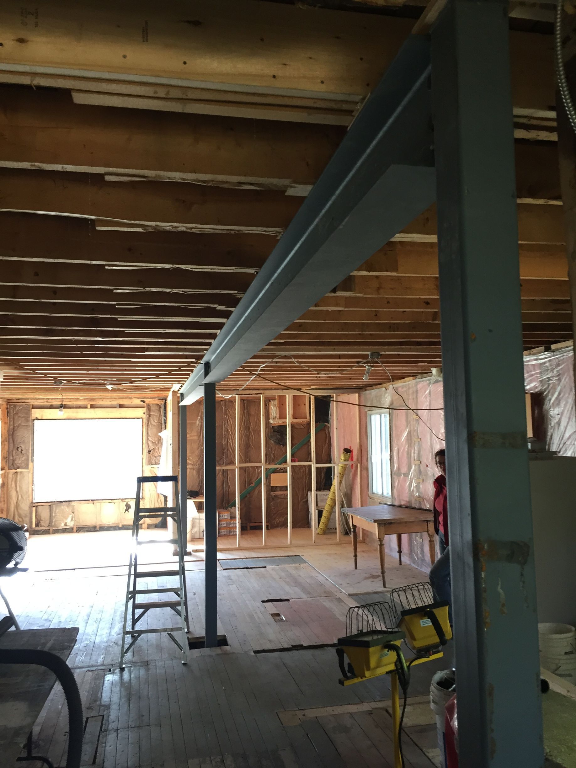 Rénovation d'une pièce avec poutres apparentes et structure porteuse métallique ; débris de construction visibles.
