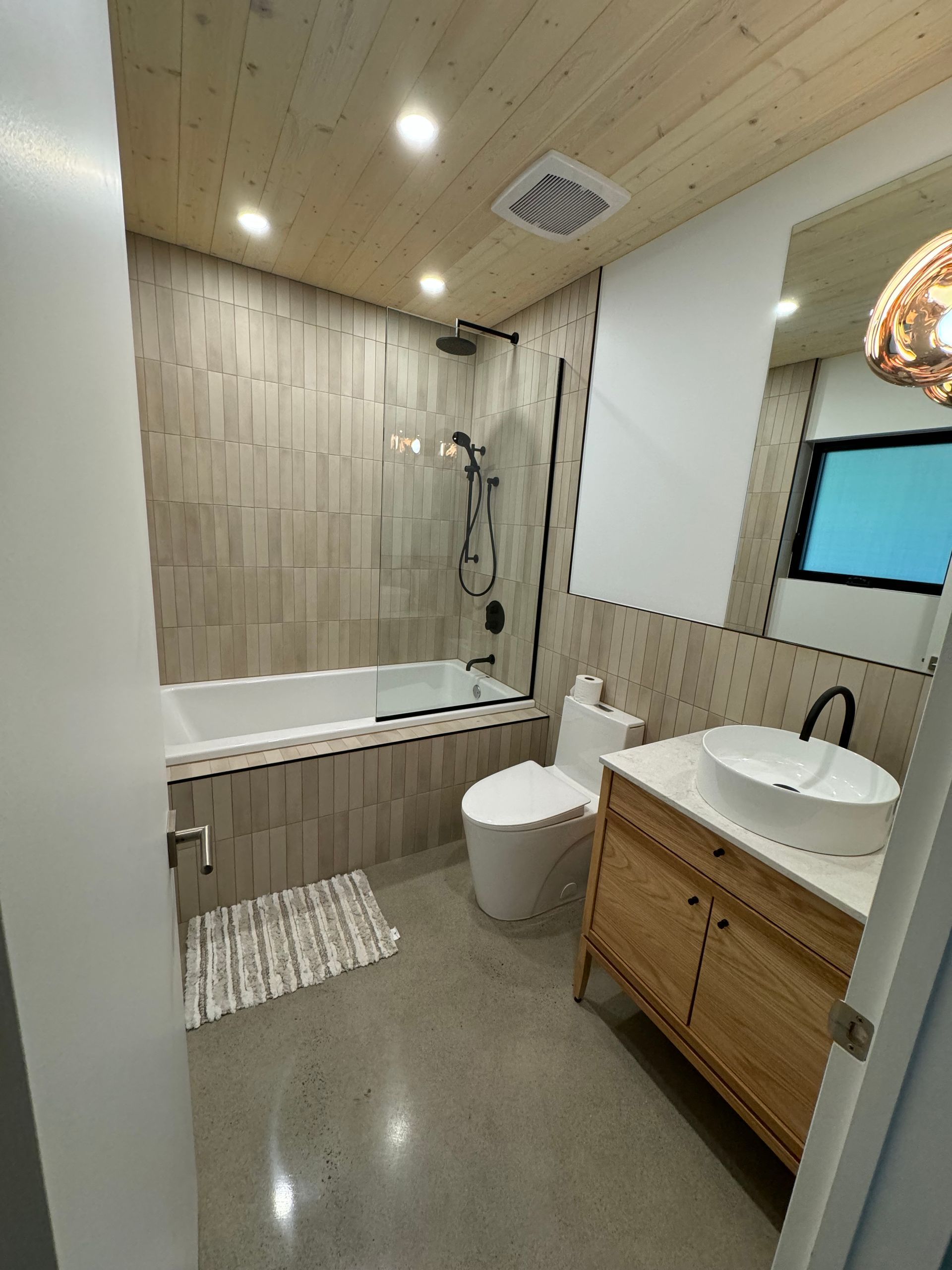 Salle de bains moderne avec plafond en bois, douche, toilettes et meuble-lavabo avec vasque.