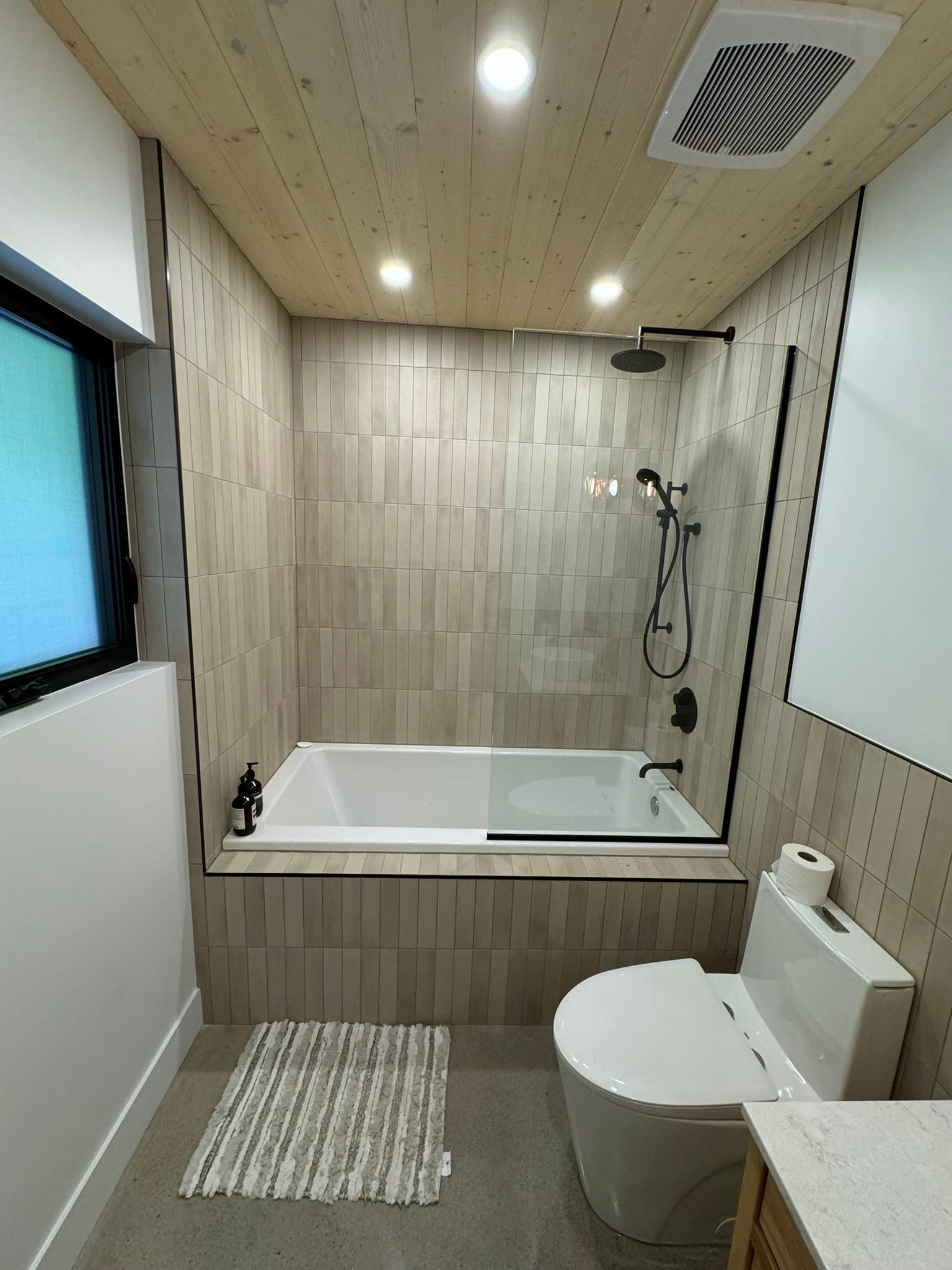 Salle de bains moderne avec baignoire, douche et toilettes, avec carrelage clair et plafond en bois.