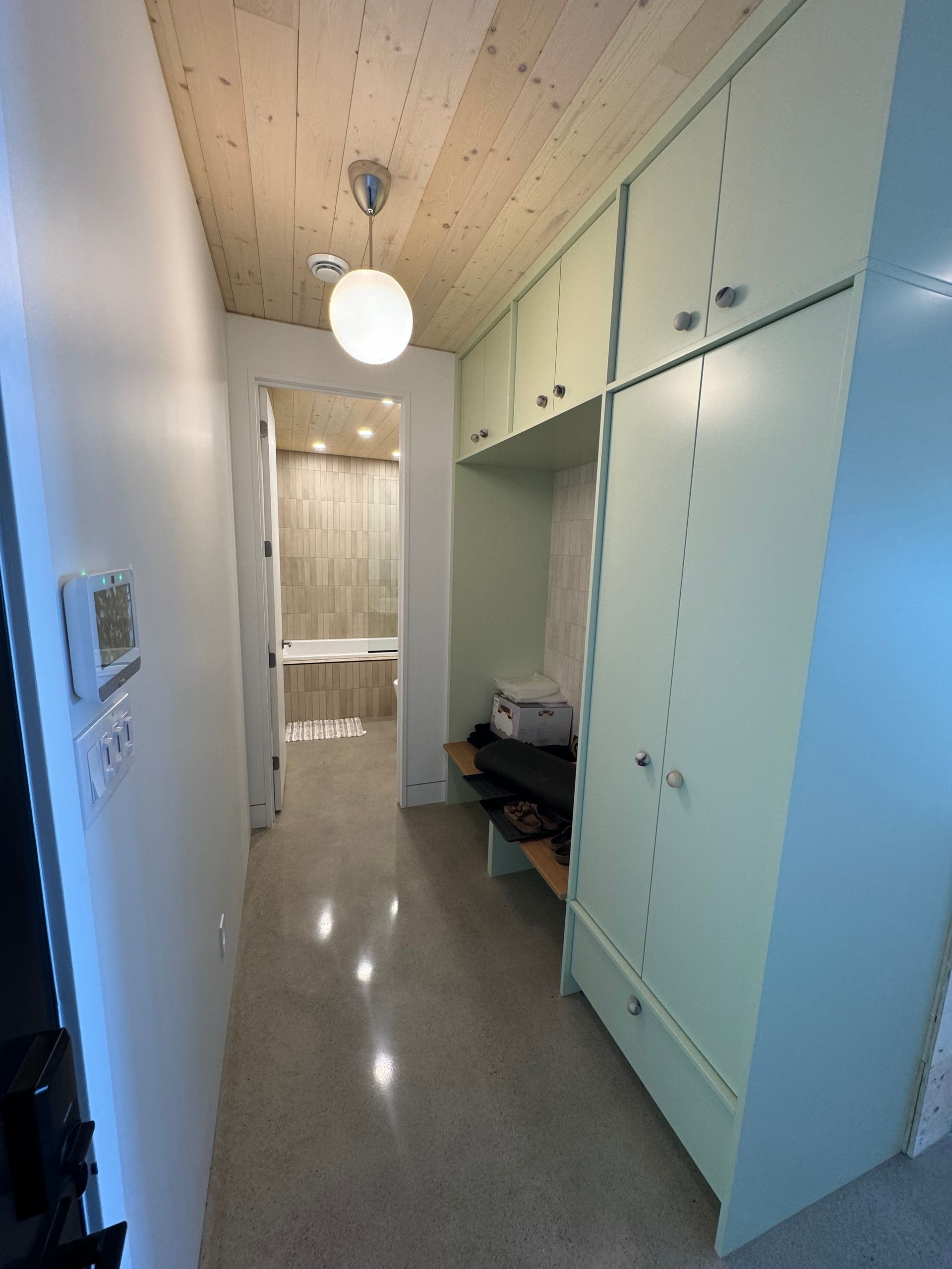 Couloir étroit avec placards vert pâle, plafond en bois et luminaire ; salle de bains visible au fond.
