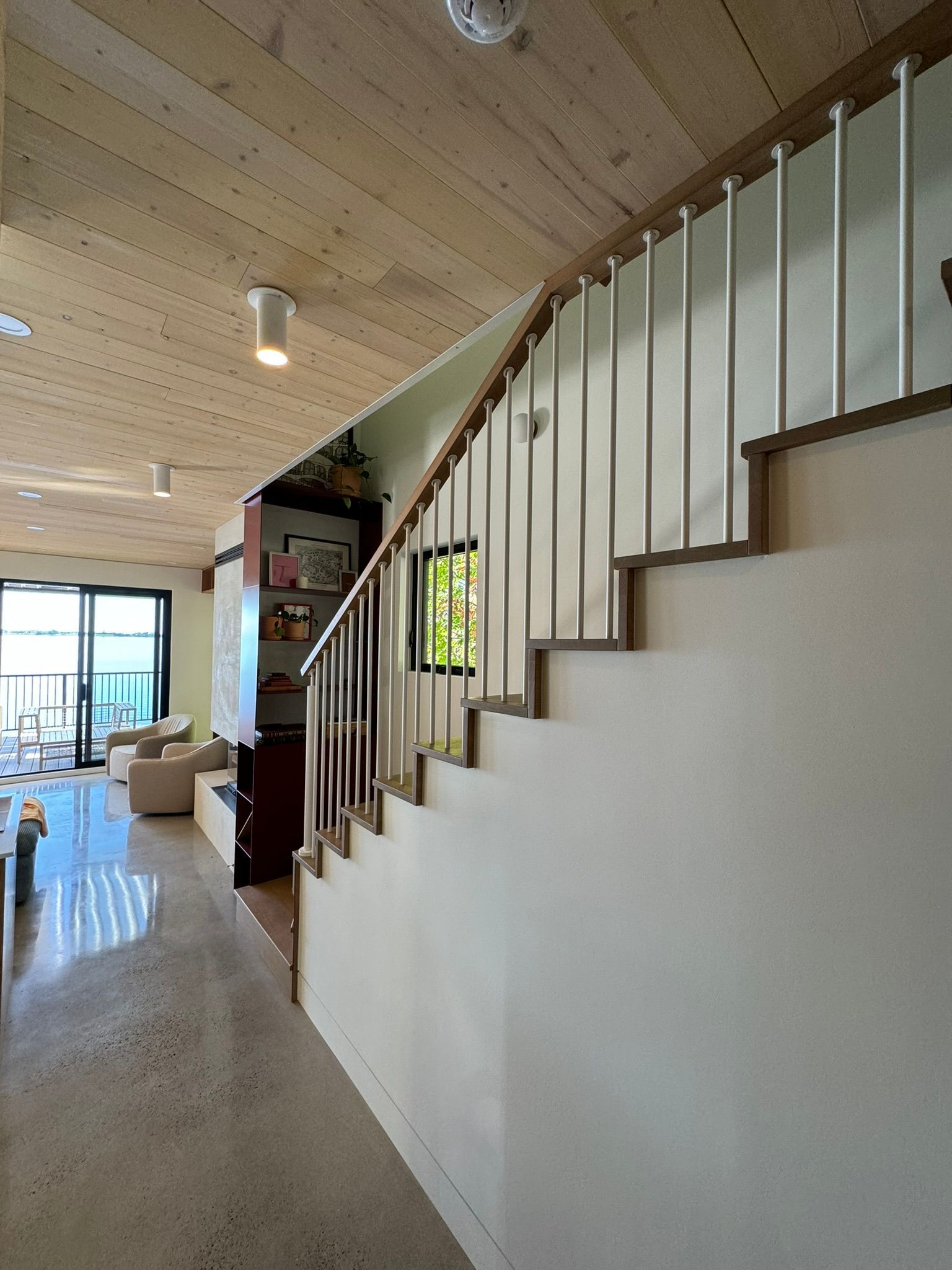 Escalier avec mur blanc, marches en bois et rampe argentée. Plafond en bois clair et sol en pierre.