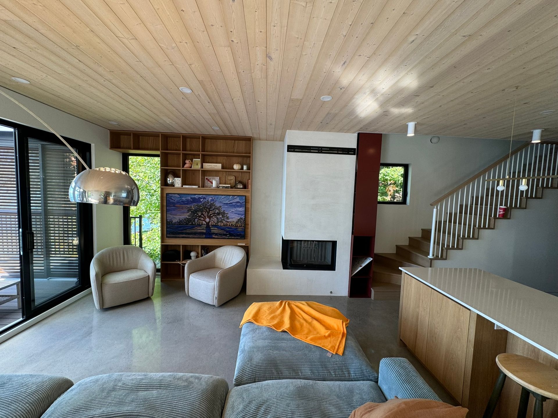 Salon avec plafond en bois, cheminée, étagères intégrées, coin salon et escalier.