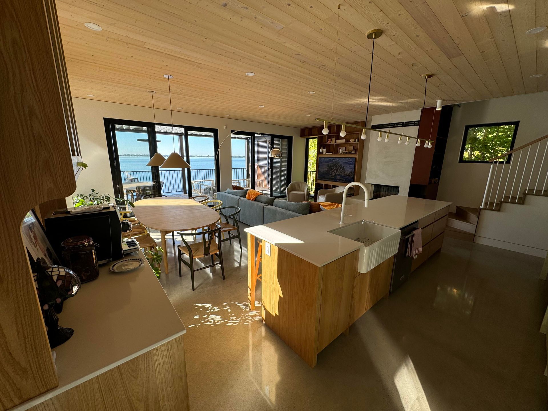 Cuisine et séjour à aire ouverte avec un grand îlot central, un plafond en bois et une vue sur l'eau à travers des portes coulissantes.