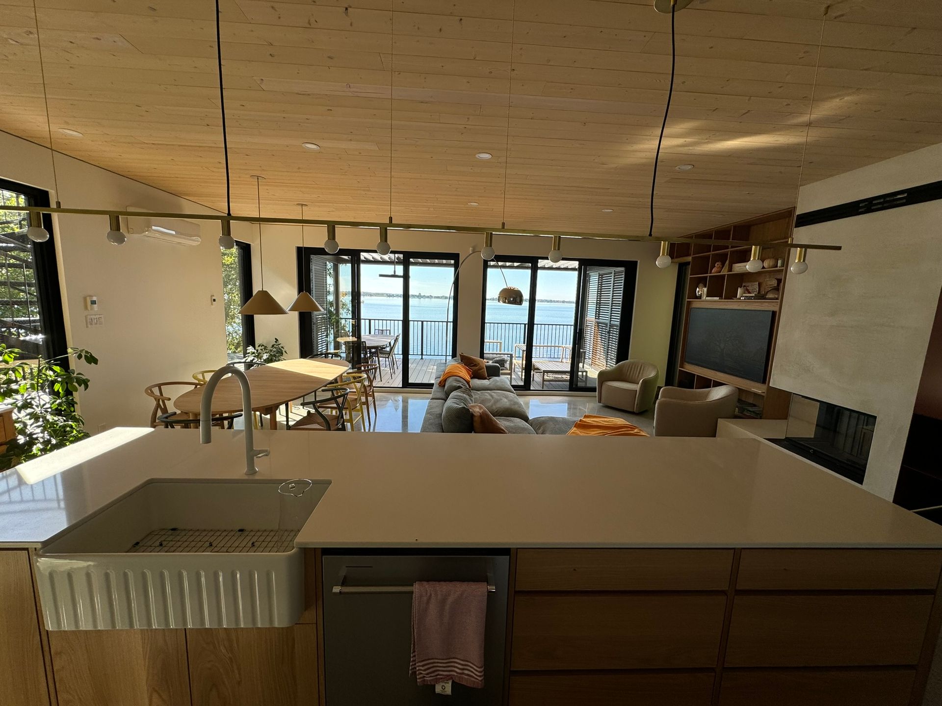 Cuisine avec îlot central, évier et vue sur l'eau grâce à de grandes fenêtres. La lumière naturelle inonde l'espace.