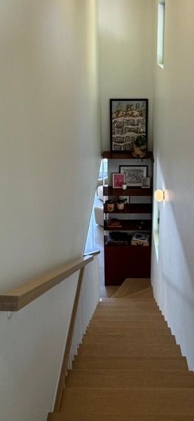 Escalier descendant, avec une rampe en bois et des étagères au bout du couloir.