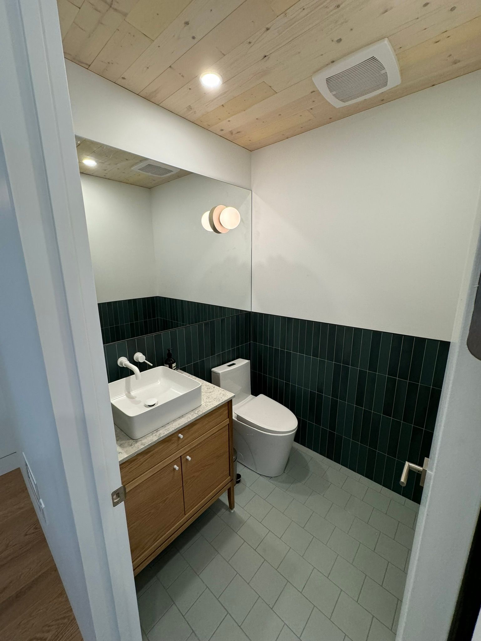 Des toilettes modernes avec un plafond en bois, un lavabo vasque carré et un mur d'accent en carrelage vert.