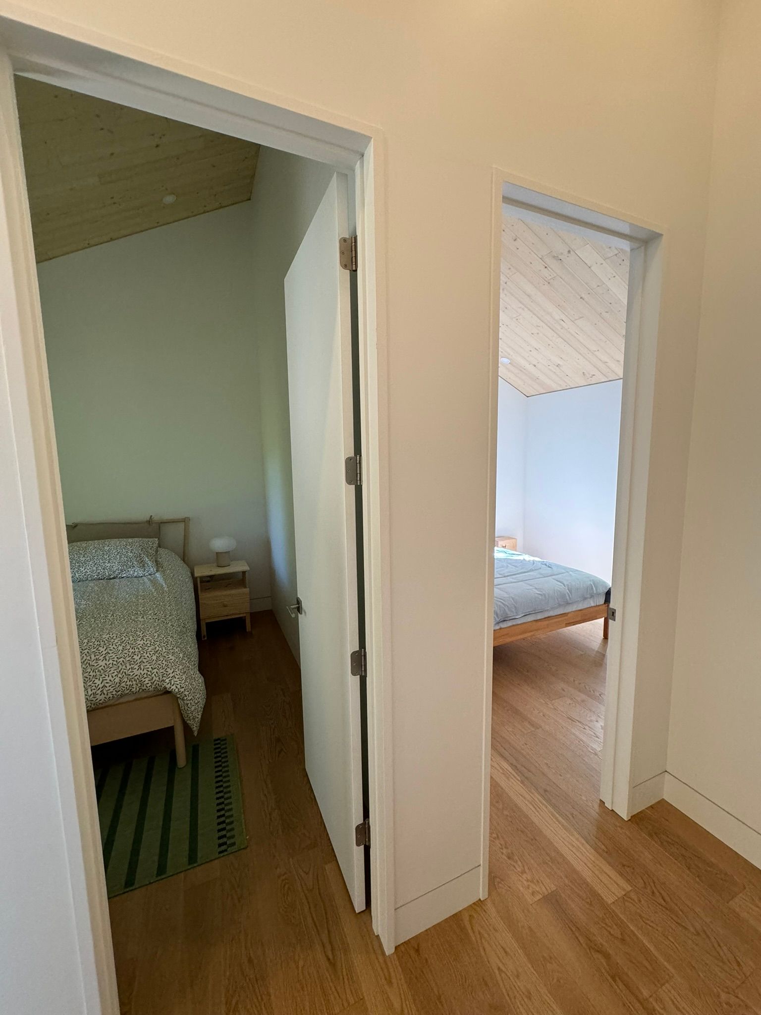 Deux chambres visibles depuis le couloir ; portes blanches, parquet clair, lit dans chaque chambre.