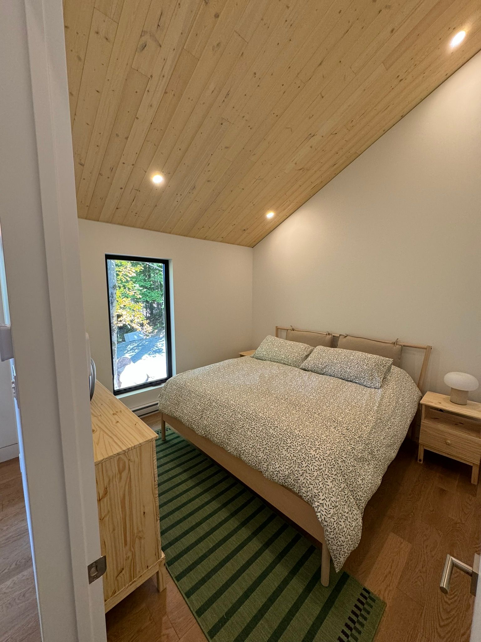 Chambre avec plafond et lit en bois, tapis vert, meubles en bois, fenêtre avec vue sur l'extérieur.