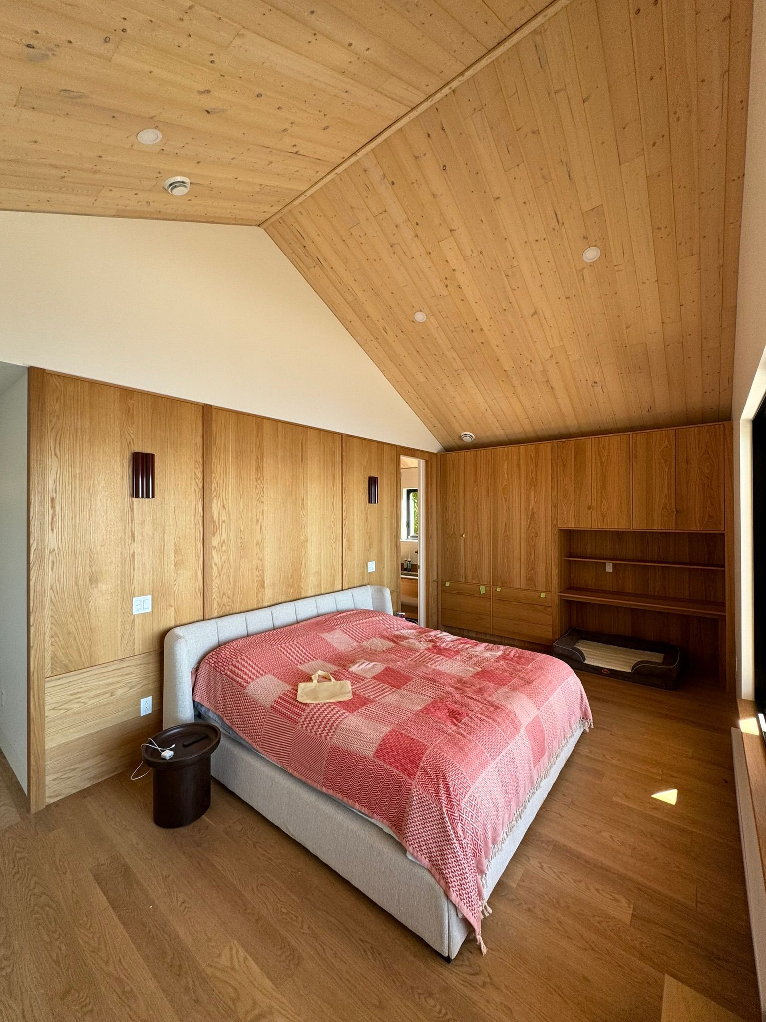 Chambre avec murs et plafond en bois, un lit avec une couverture rouge et une table de chevet.
