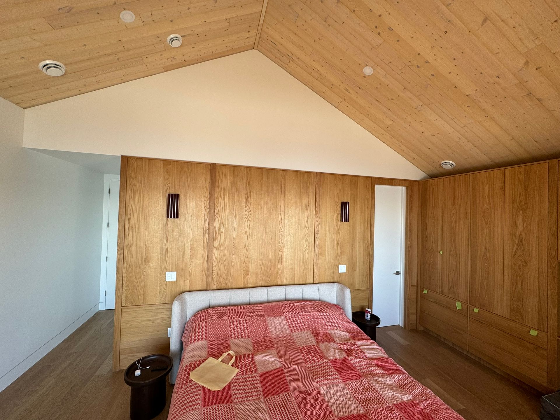 Chambre avec lambris et plafond mansardé. Couette rouge à motifs sur le lit. Murs blancs.