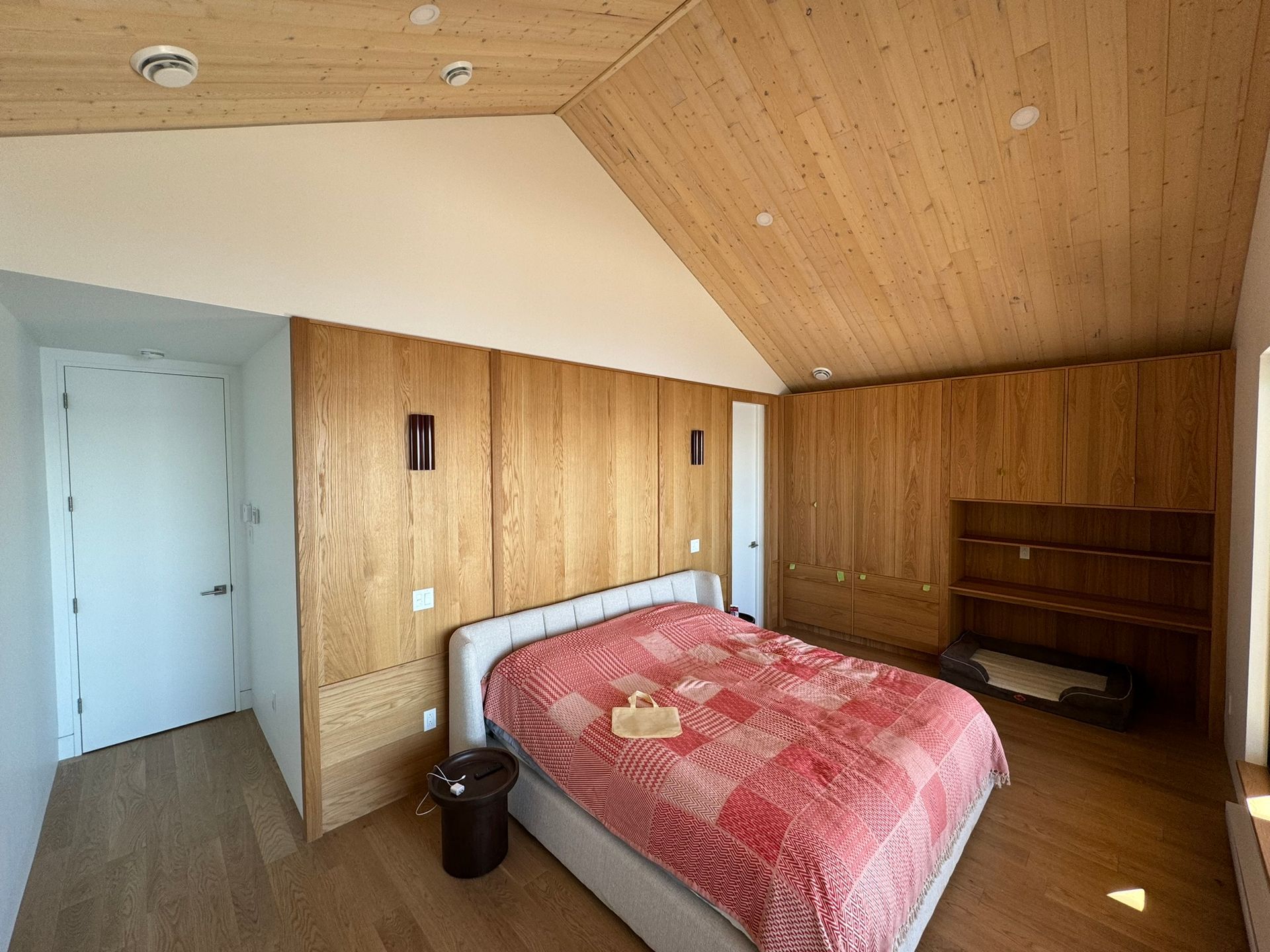 Chambre avec lambris, un lit recouvert d'une couette rouge et une porte blanche fermée.
