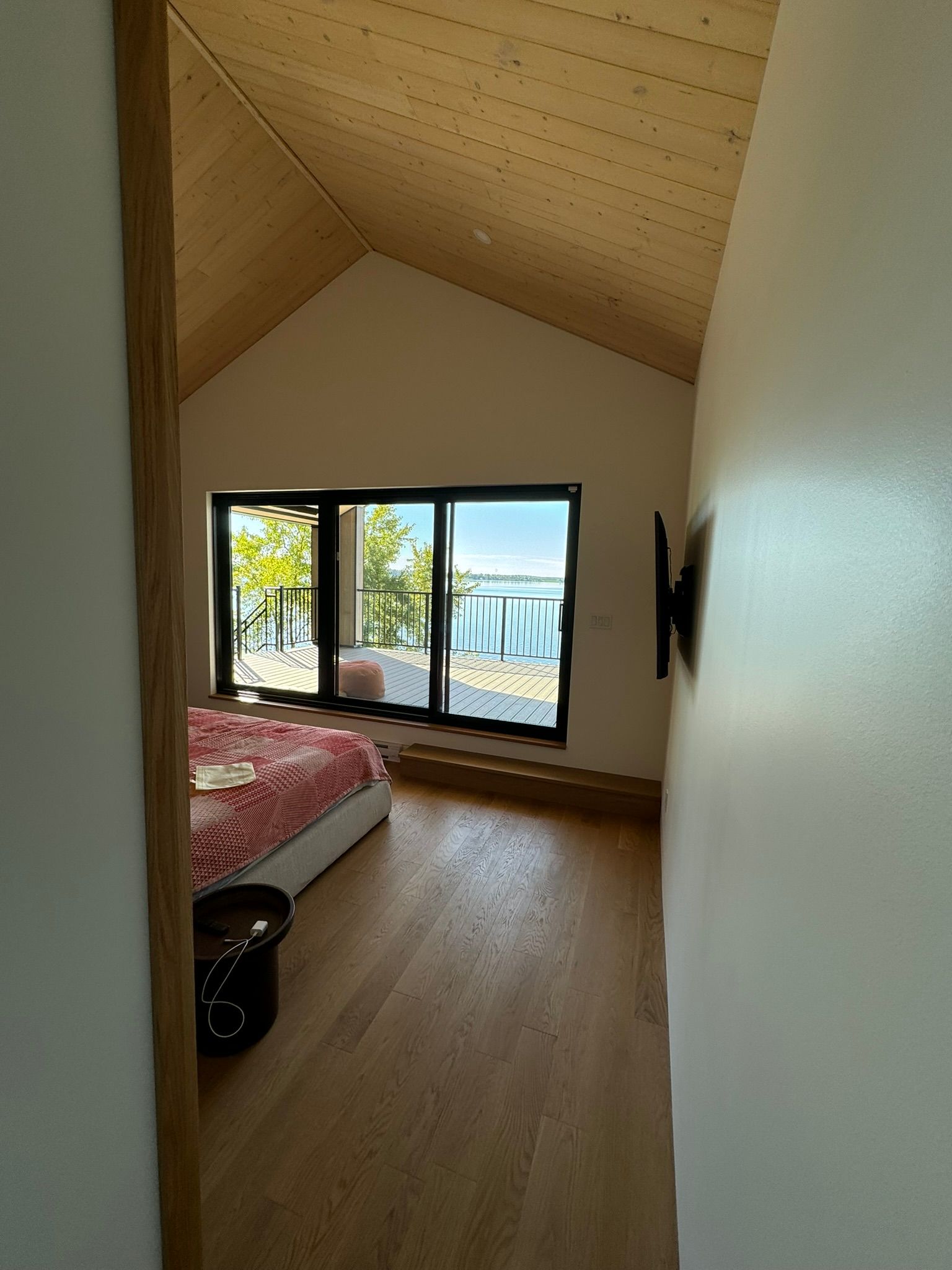Chambre avec parquet, plafond mansardé, grande fenêtre donnant sur le lac. Lit avec couverture rose.