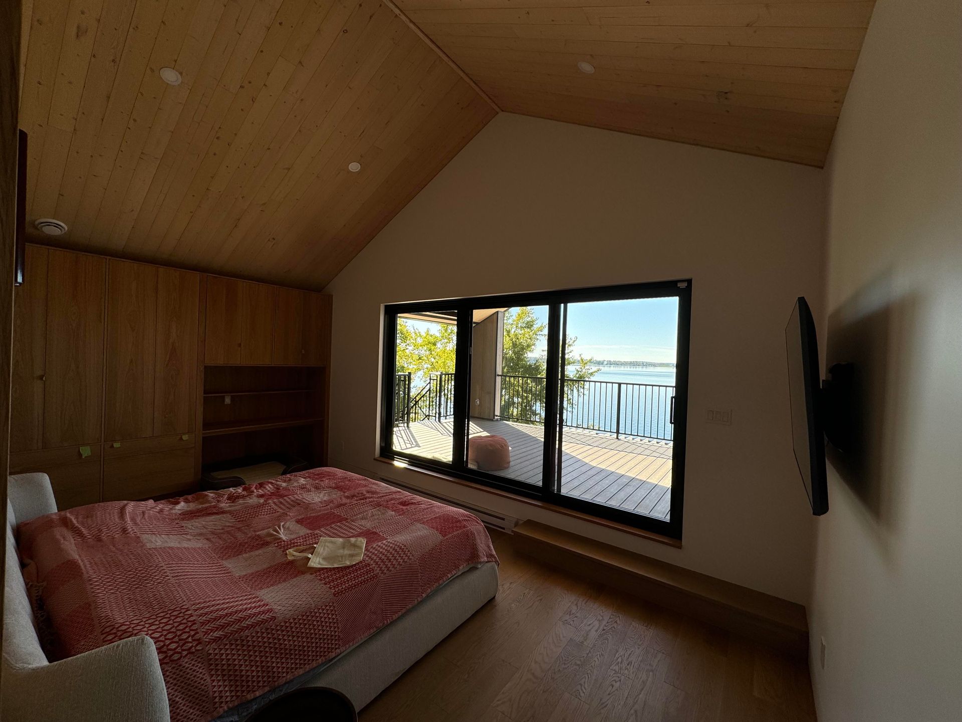 Chambre avec lit, placard et grande fenêtre donnant sur un plan d'eau.